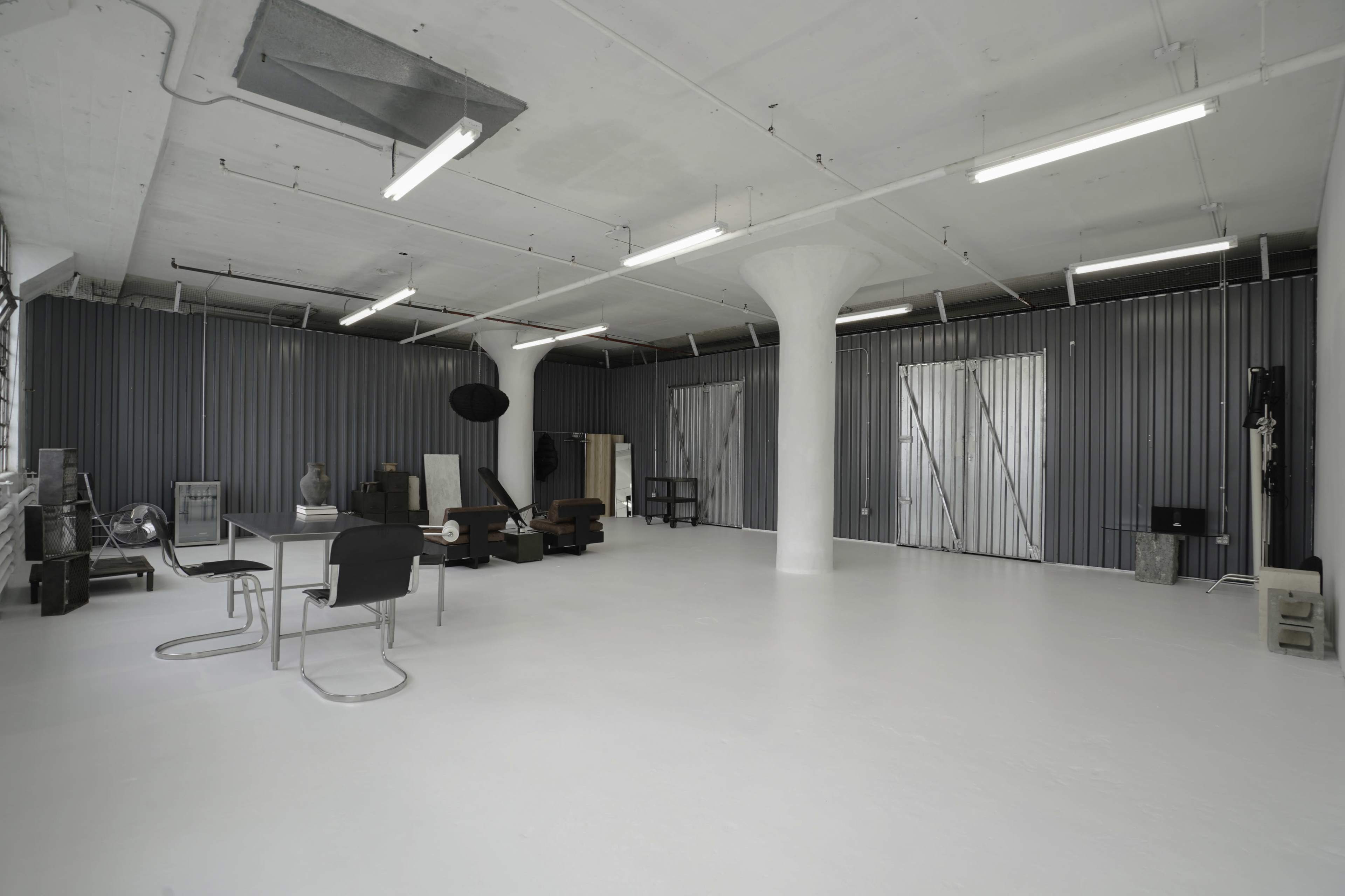 A spacious, minimalist studio with white floors, industrial gray walls, and various pieces of furniture arranged throughout.