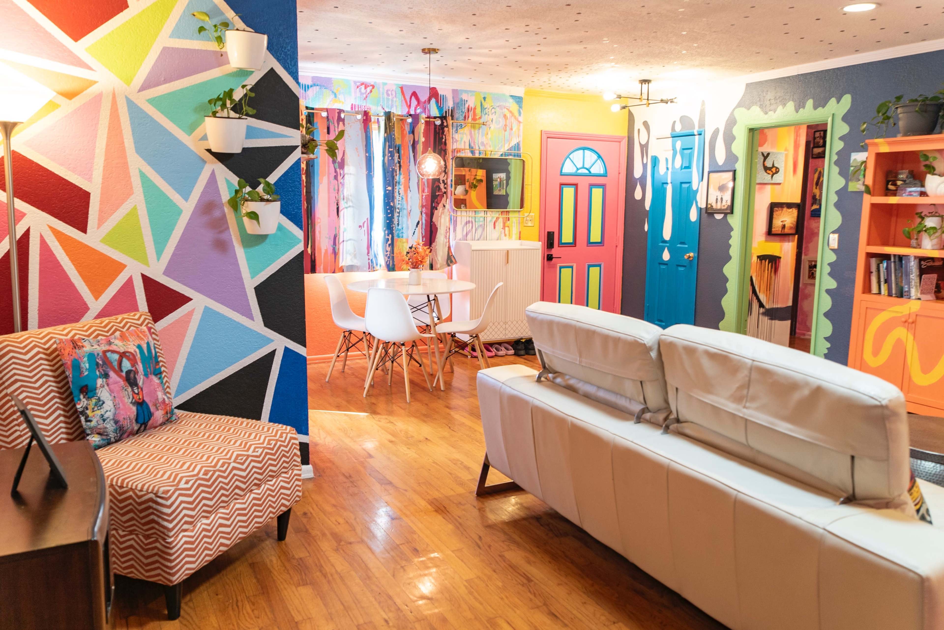 The image shows a vibrant living space featuring colorful walls, a modern white sofa, and a dining area with a round table and chairs.