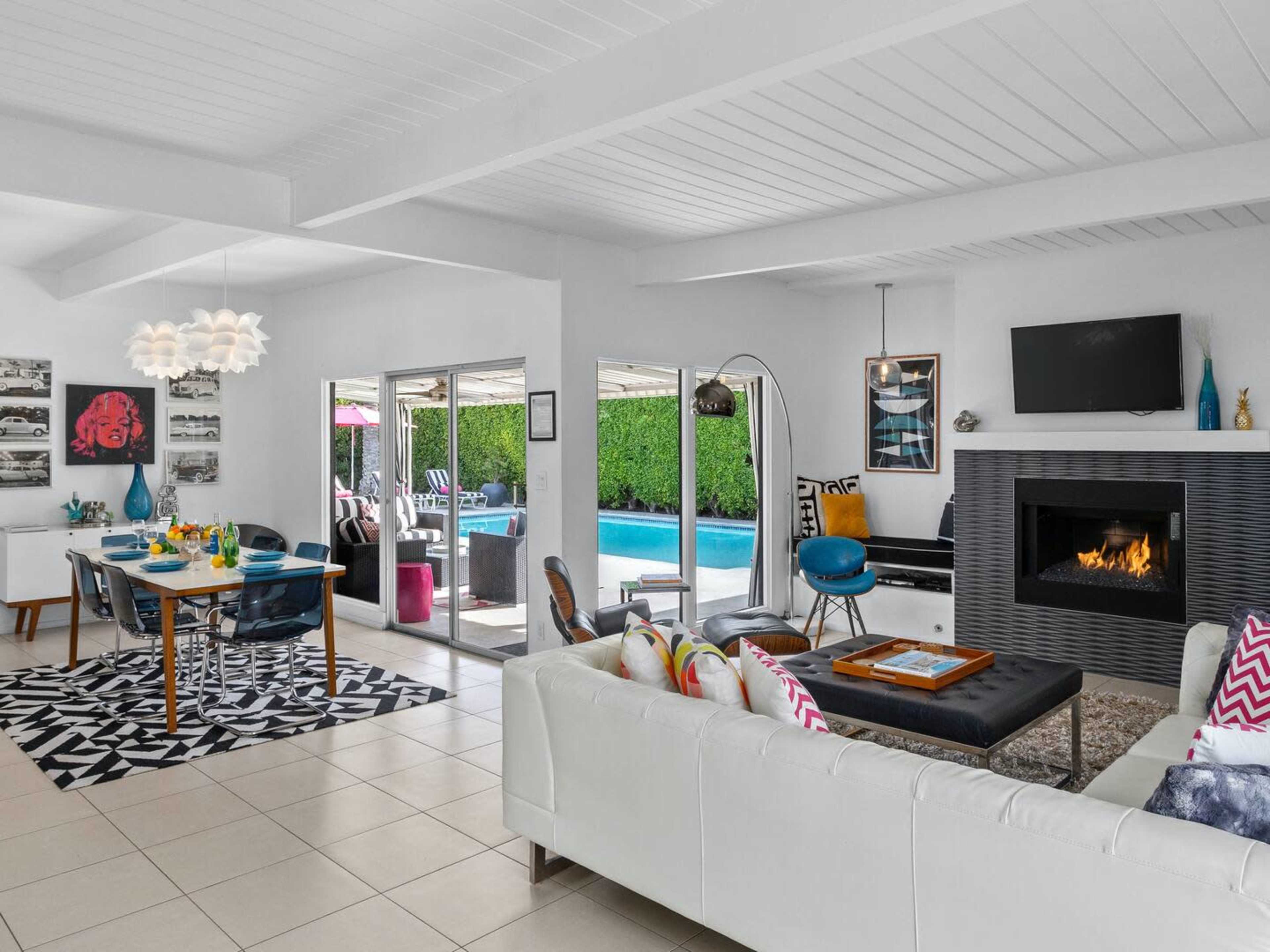 A modern living space featuring a white sofa, a dining area, a fireplace, and large sliding doors leading to a poolside patio.