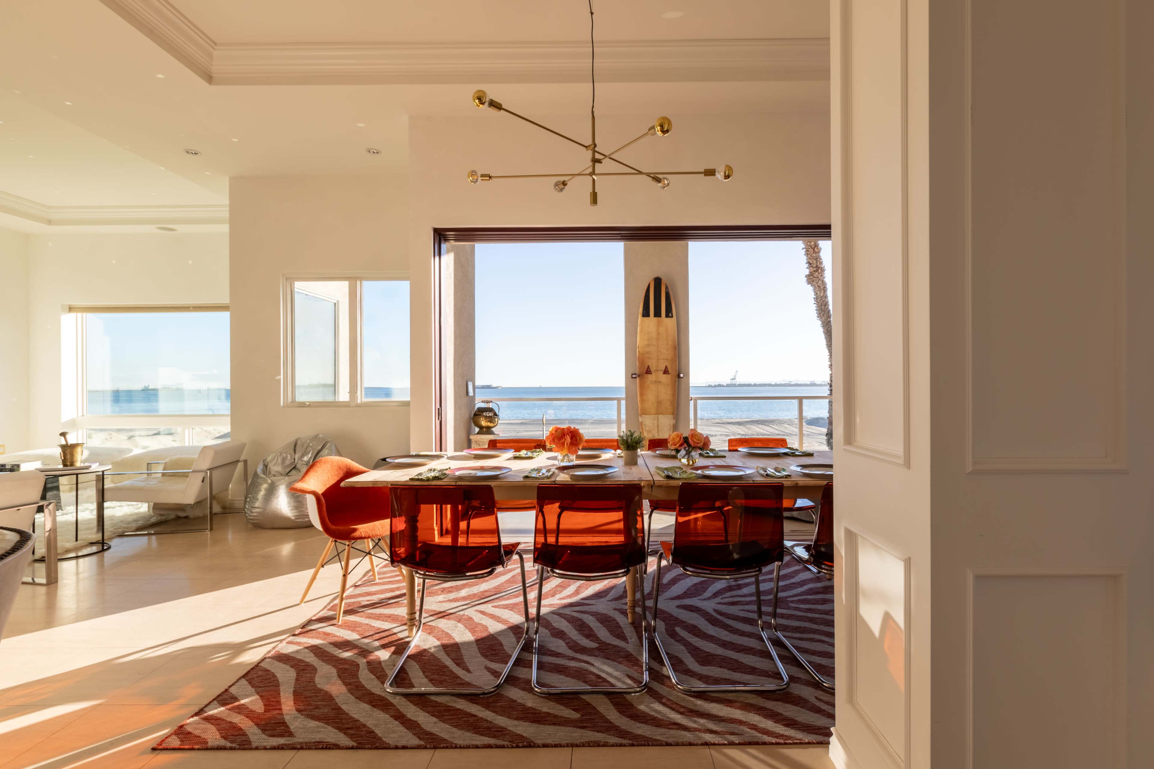 A dining area features a modern table set for a meal, with views of the ocean visible through large windows.
