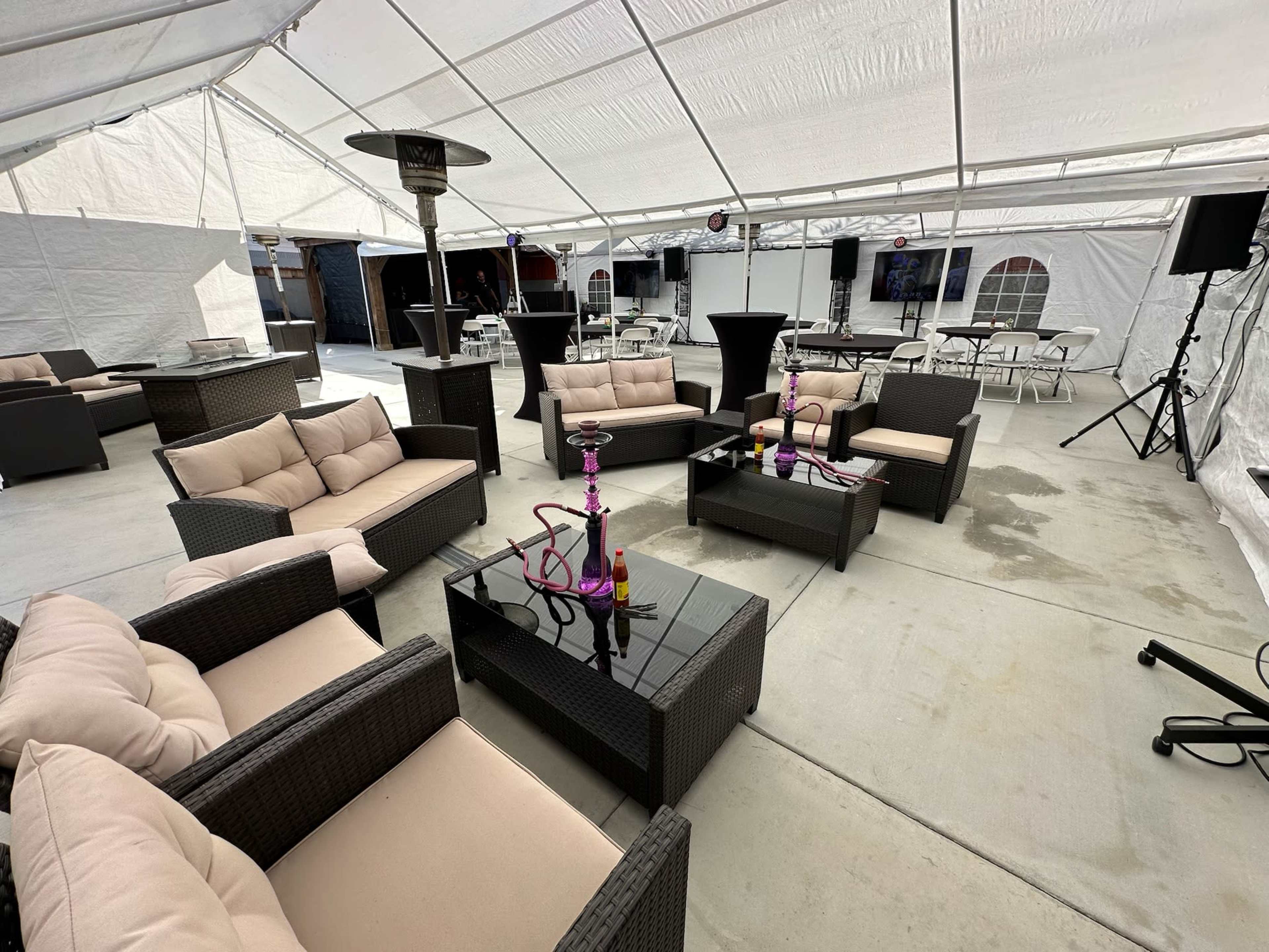 A spacious tent setup features several lounge areas with cushioned seating, a coffee table, and a hookah in the center.