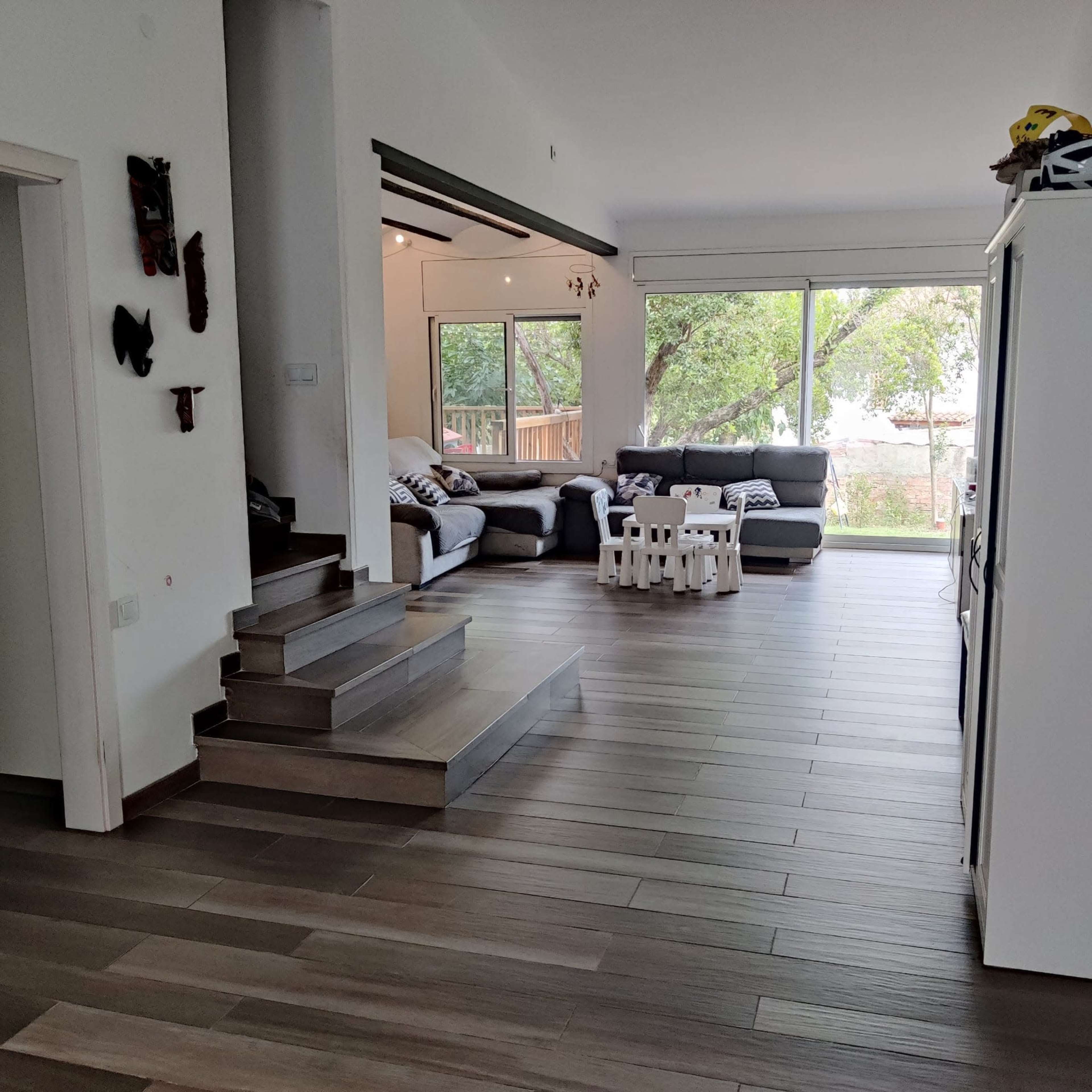 A spacious living room with a seating area, large windows, and a staircase leading to a slightly elevated floor.