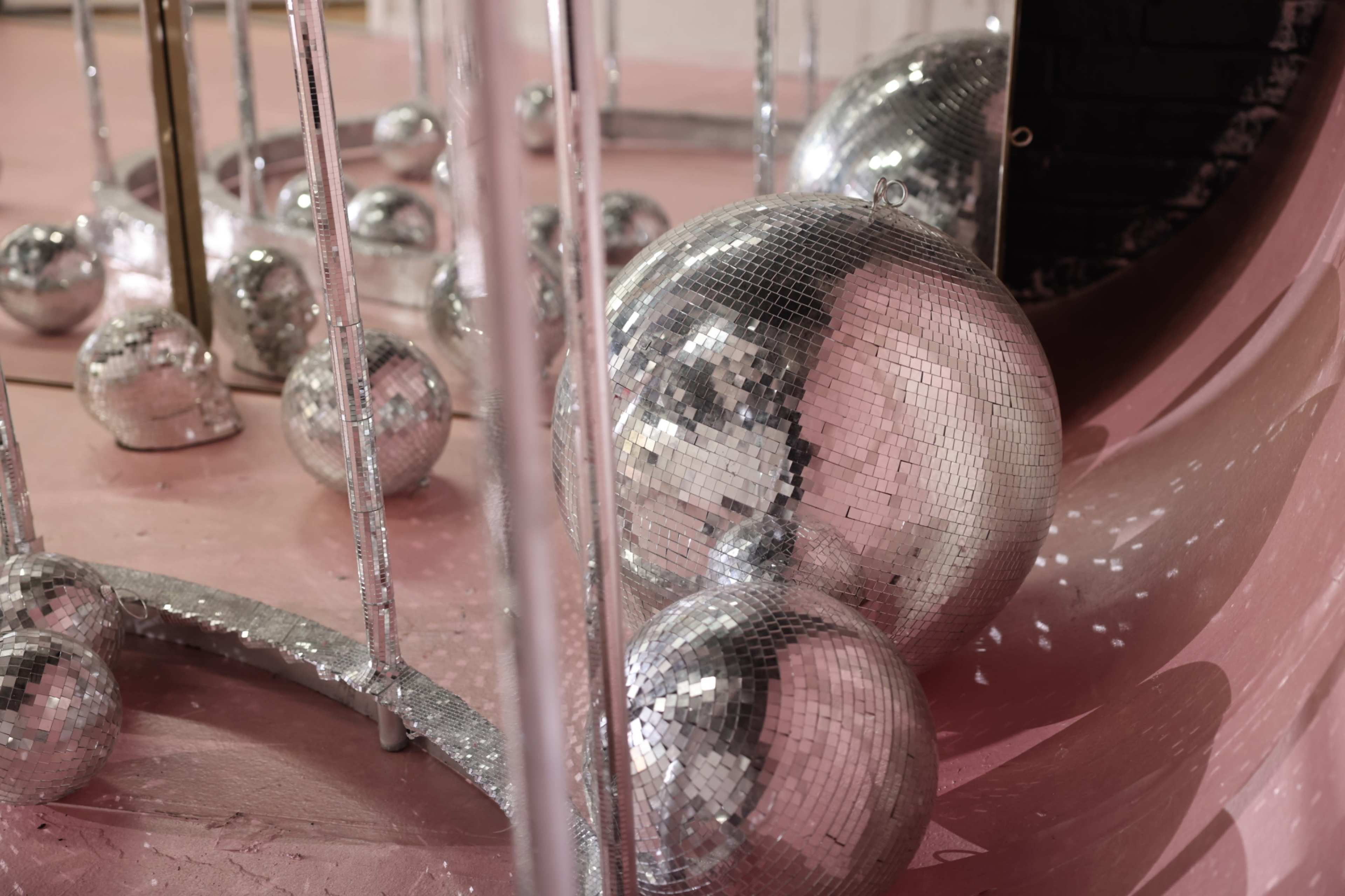 The image features several sparkling disco balls of varying sizes placed on a pink surface, reflecting light in a room with a curved wall.