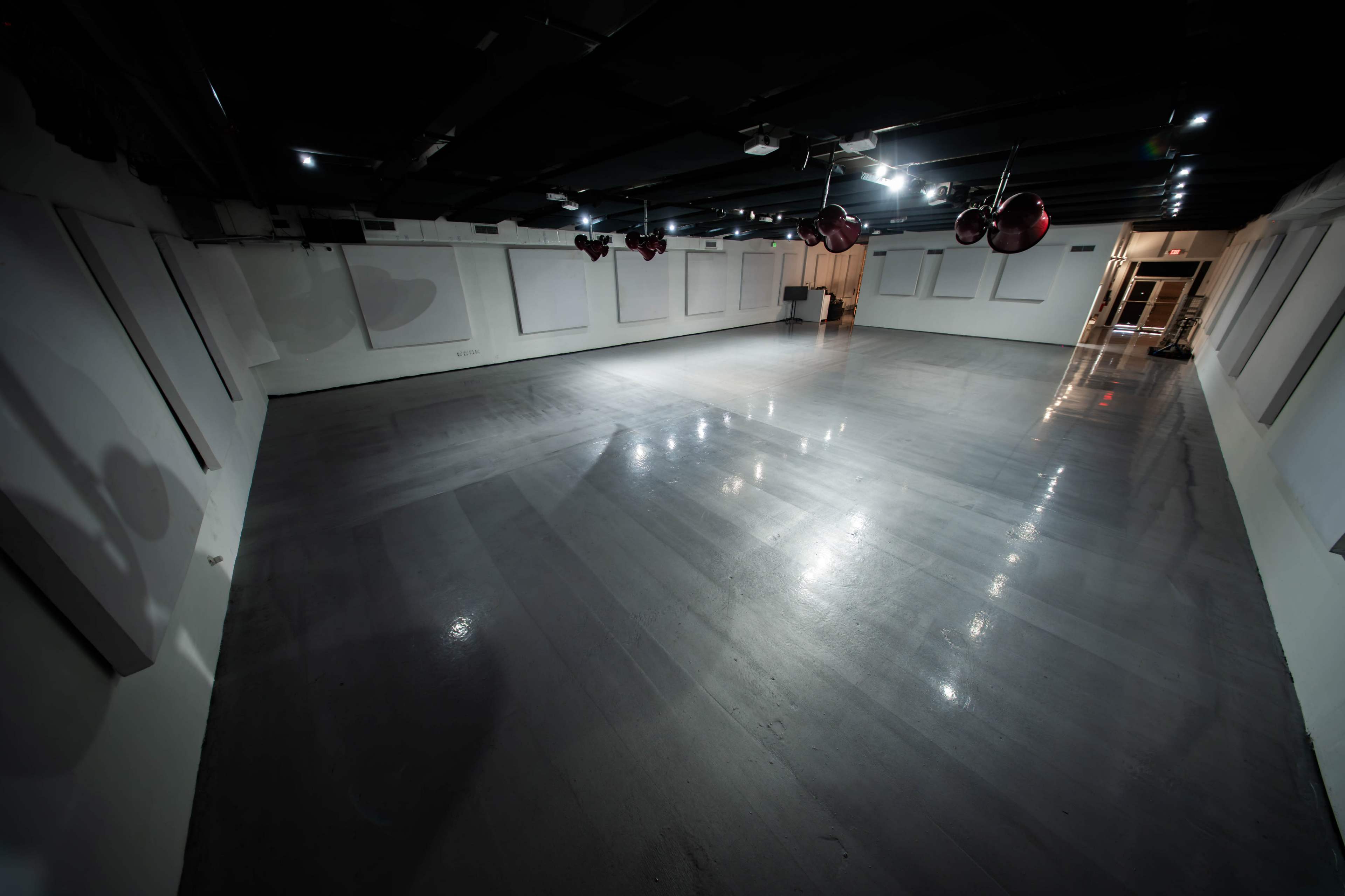 The image shows a large, empty room with a polished gray floor and a ceiling featuring several hanging red ornaments.