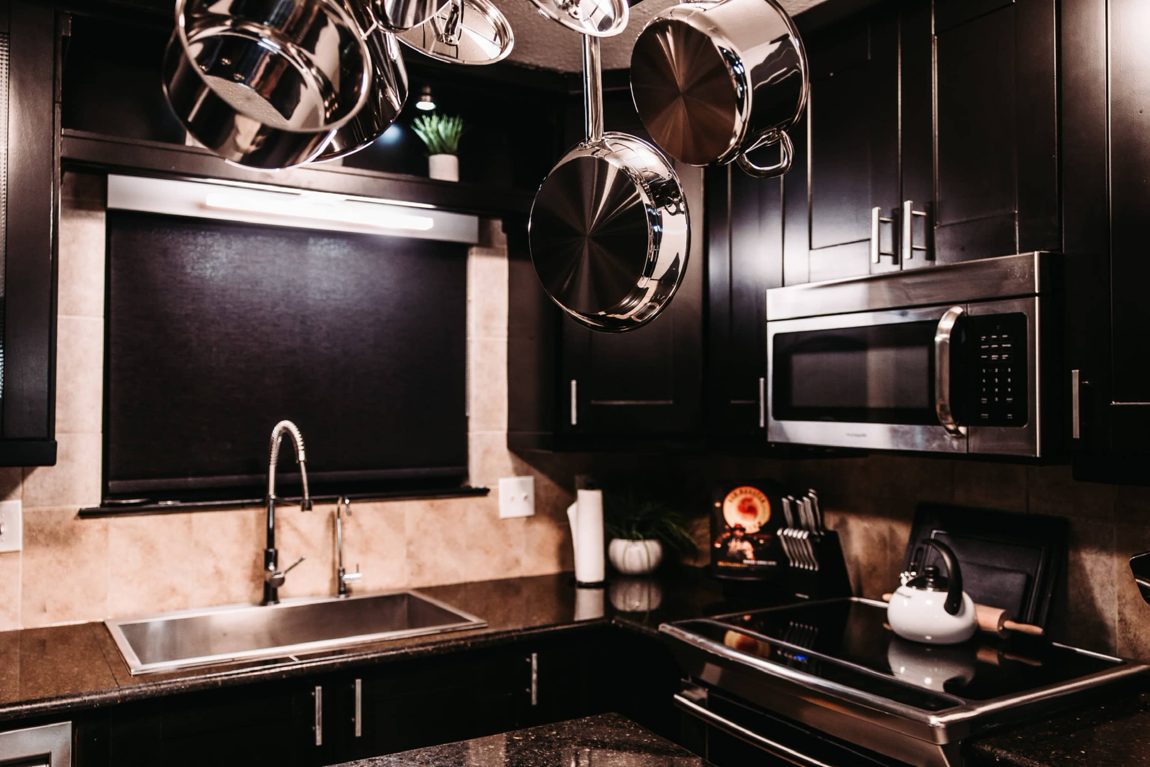 A modern kitchen features dark cabinetry, stainless steel appliances, and hanging pots above a sink and stove.