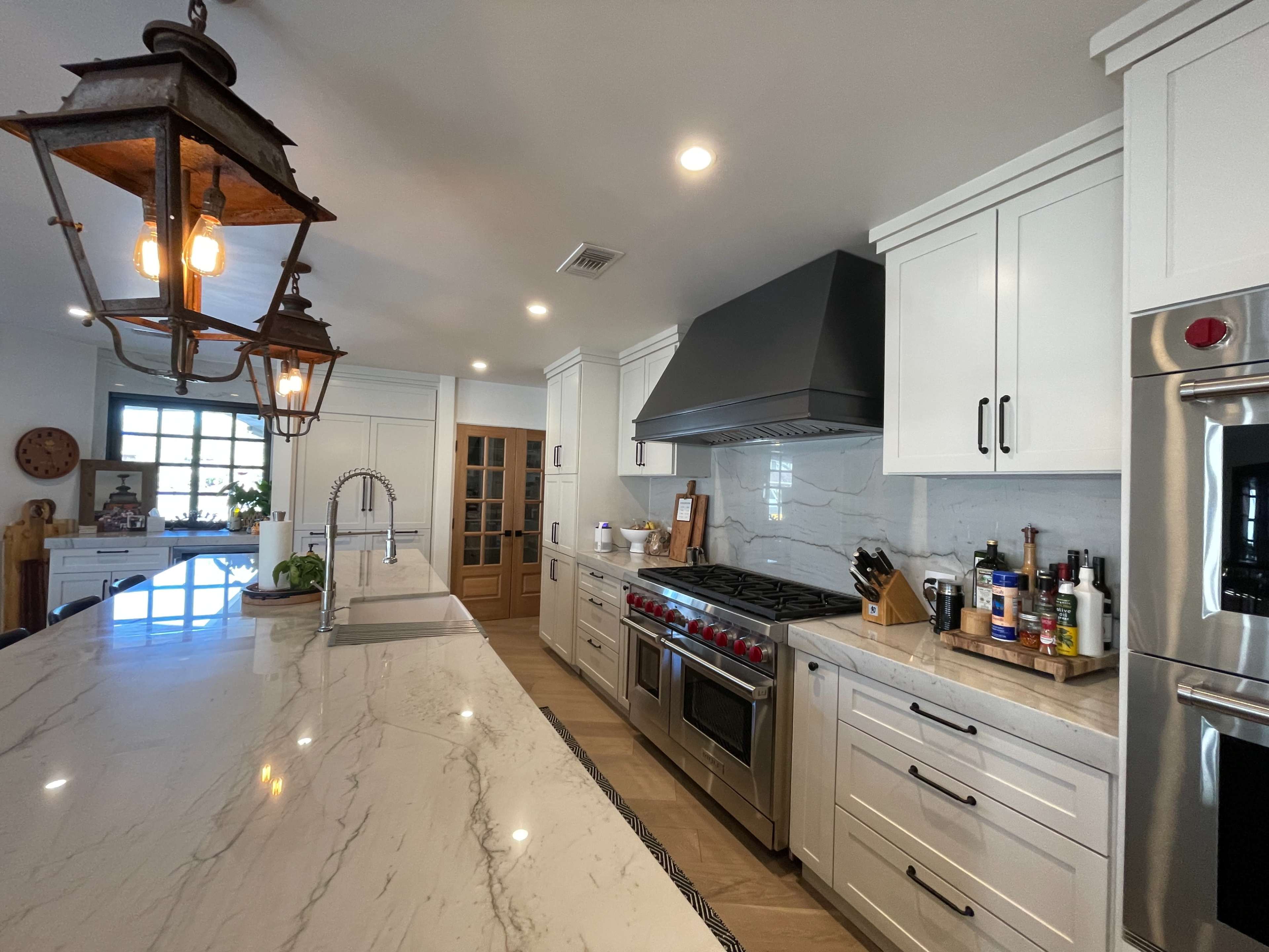 A modern kitchen featuring white cabinetry, a marble countertop, a large gas stove, and pendant lighting.