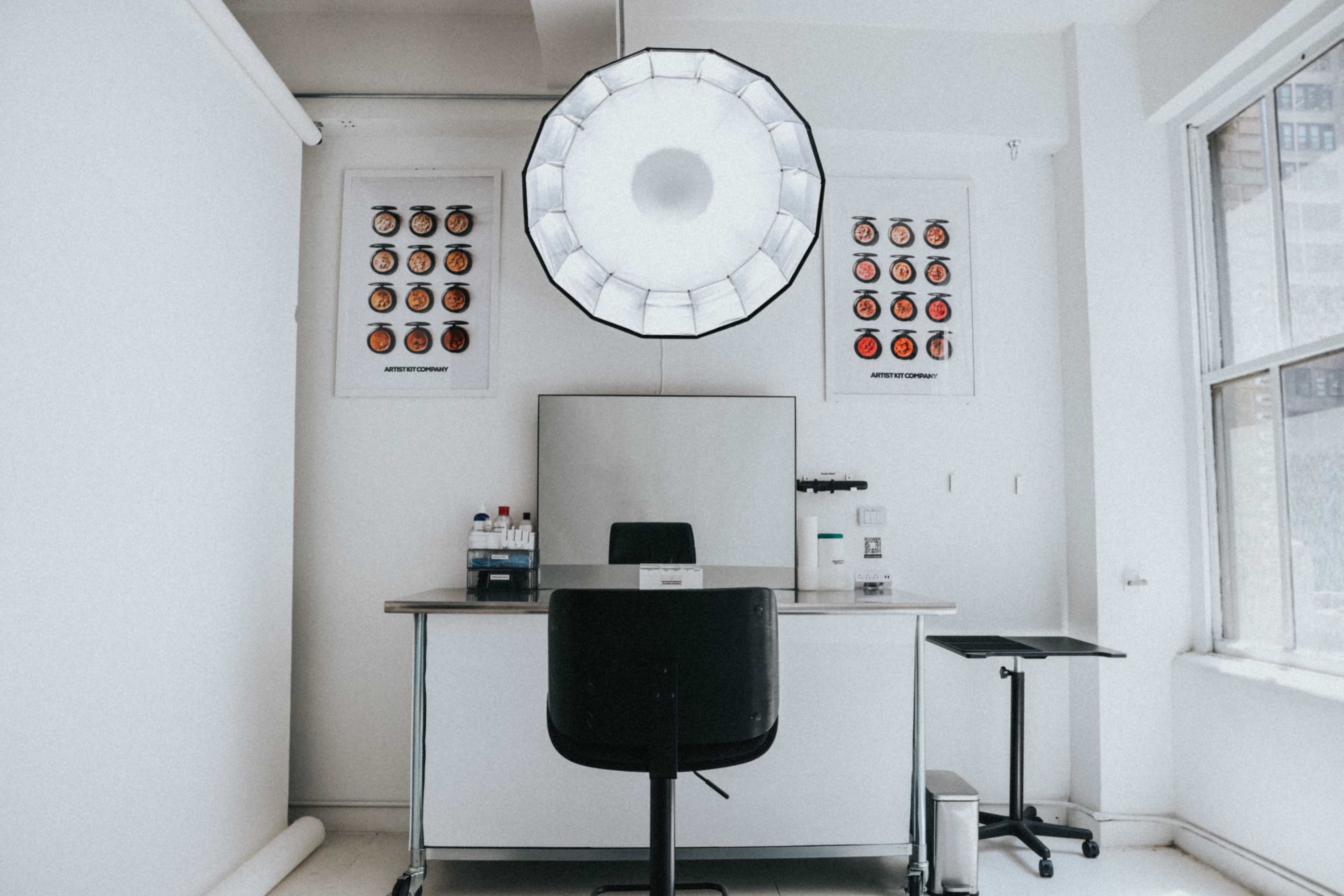 A minimalist room features a central table with a chair, an overhead light, and color palettes mounted on the wall.