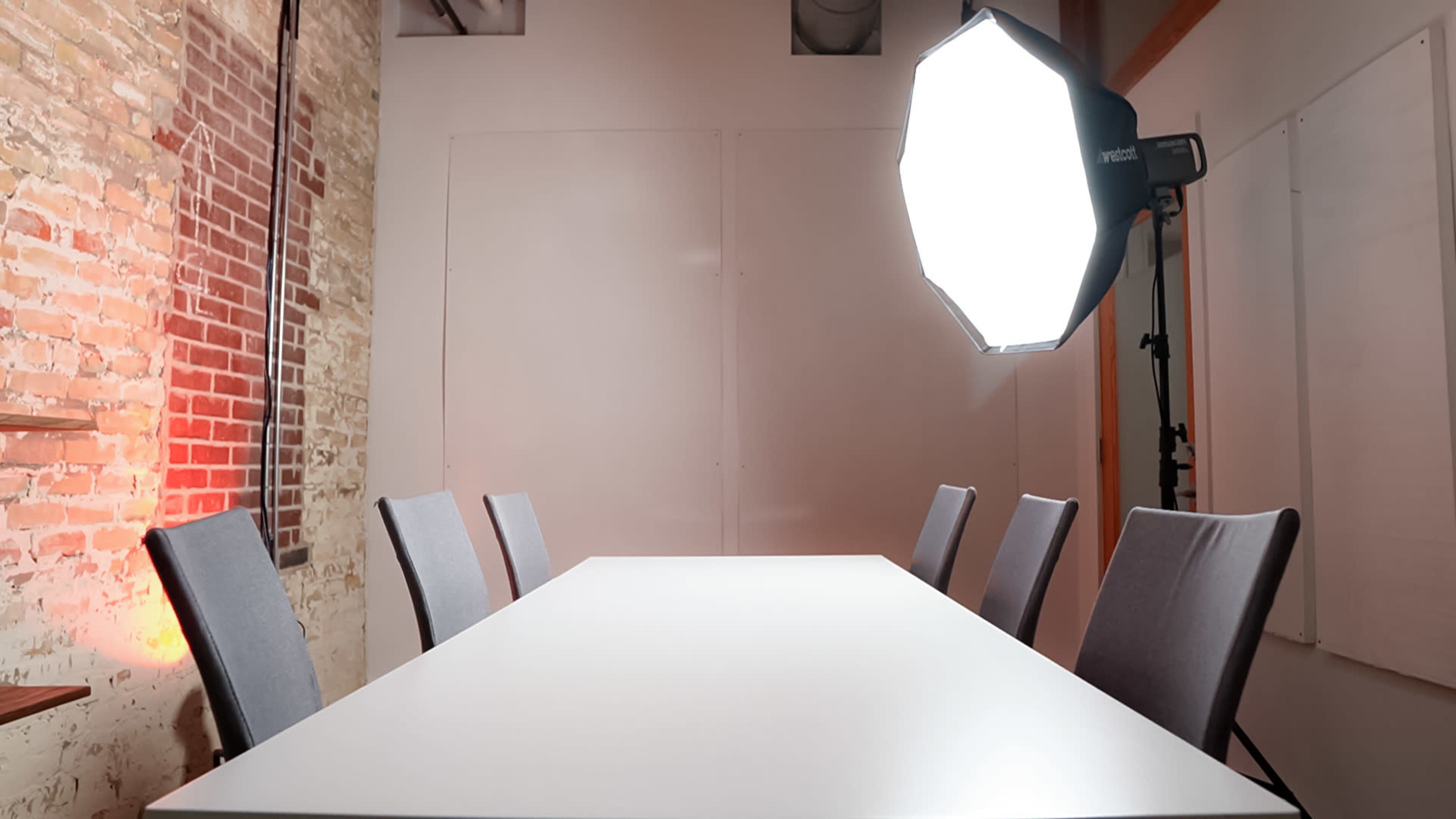 A brightly lit conference room features a long white table surrounded by gray chairs.