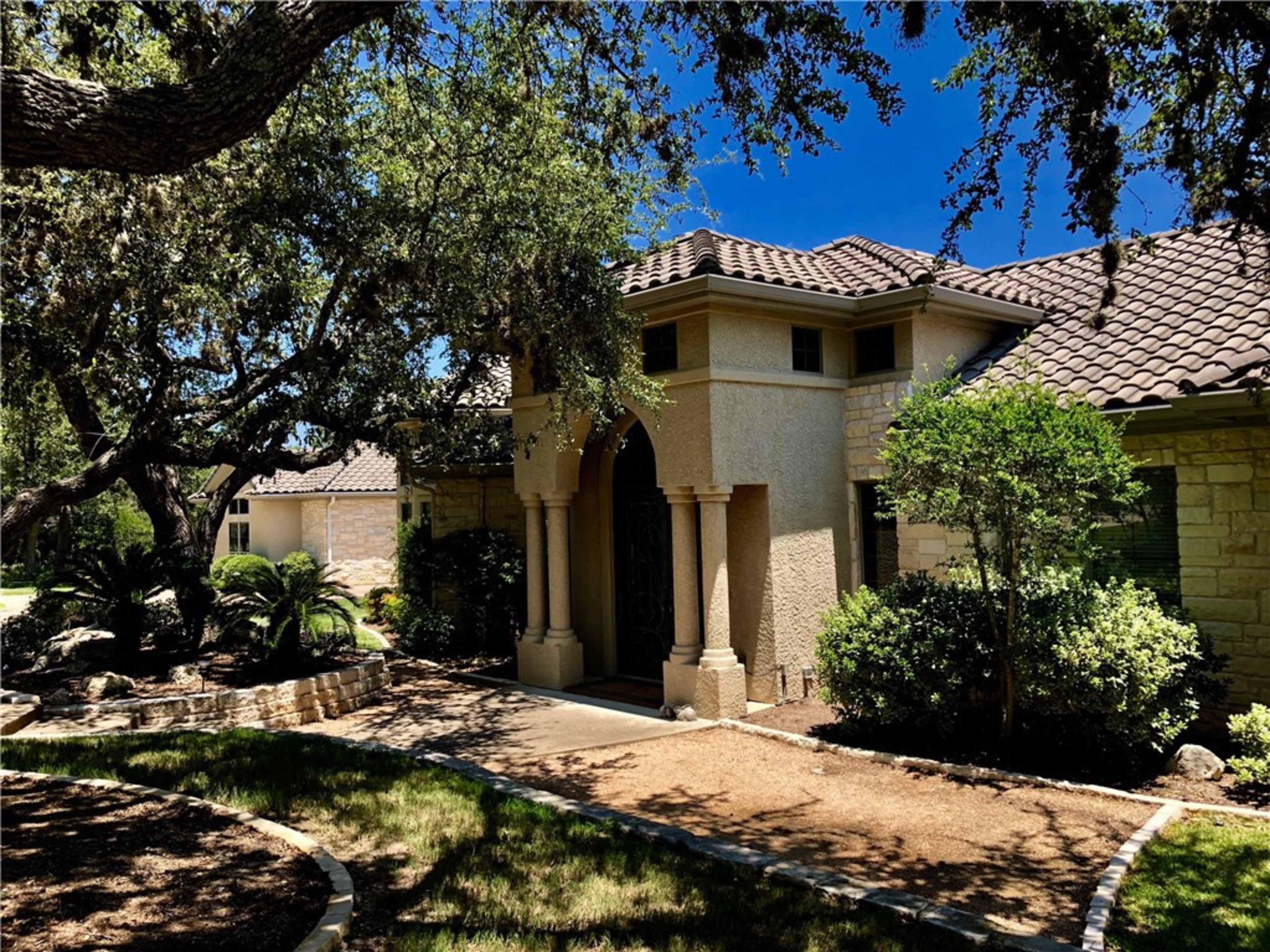 A house with a stone exterior and a tiled roof, surrounded by greenery and trees.