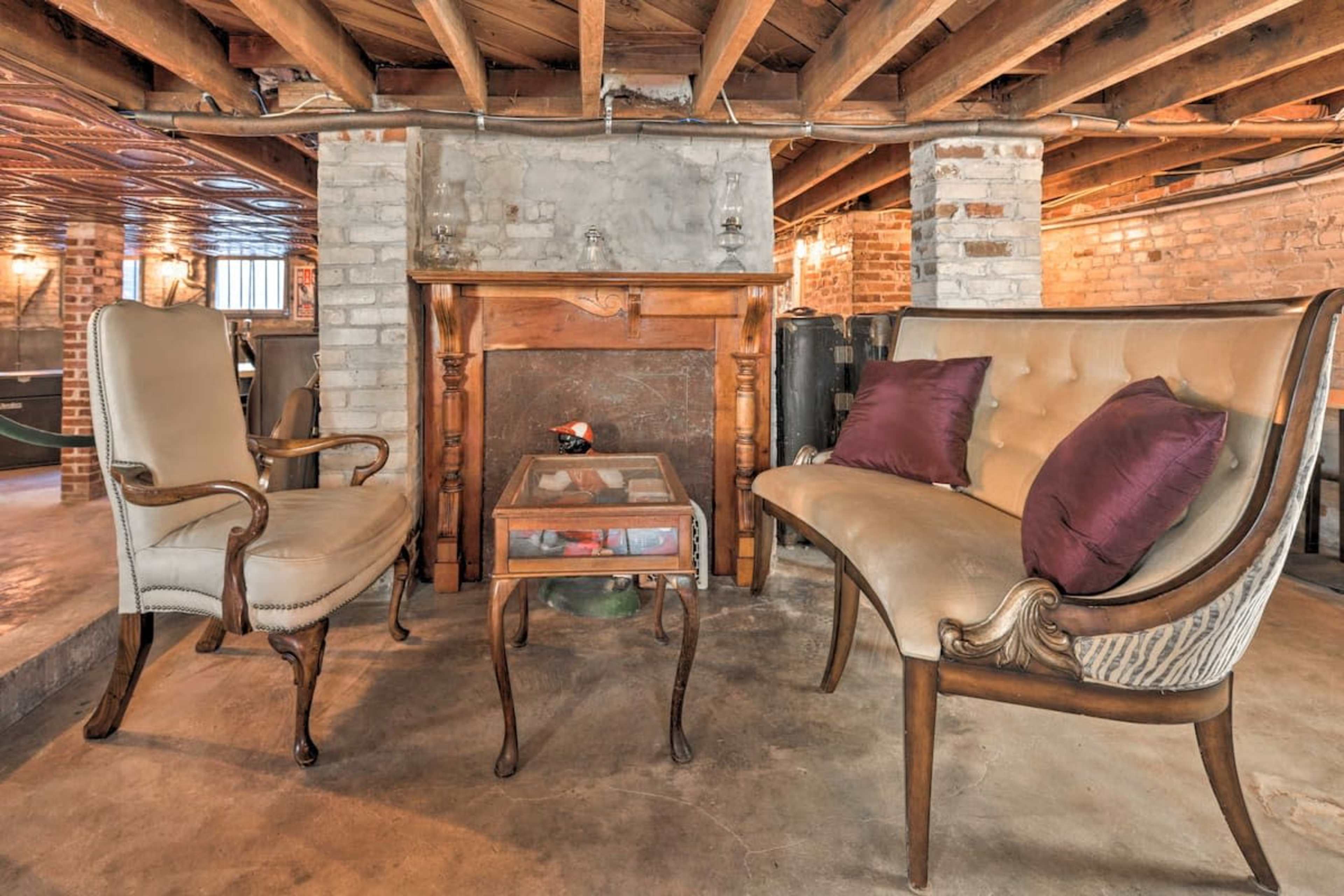 A basement area with two antique-style chairs and a wooden table positioned in front of a brick fireplace.