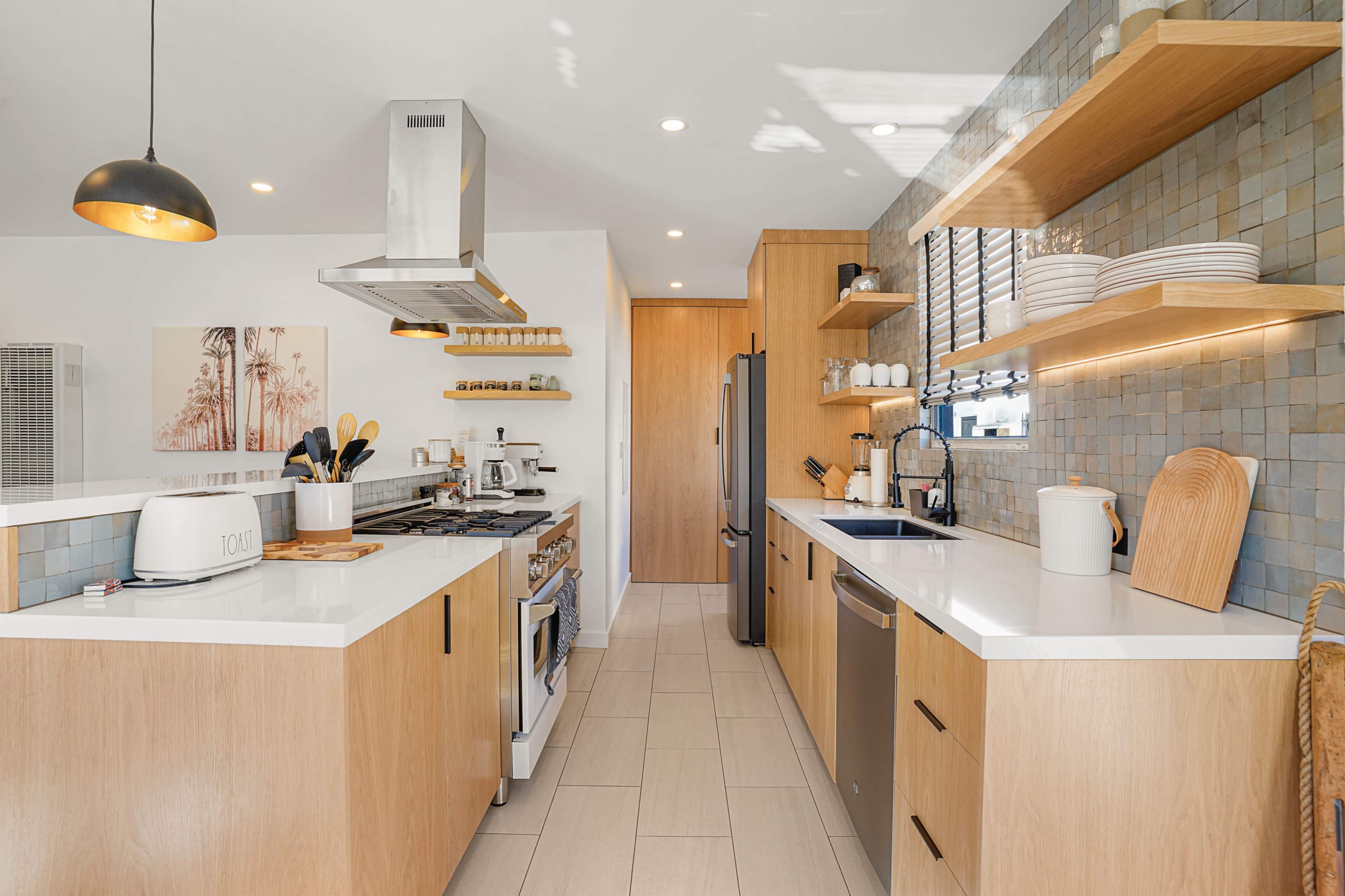 A modern kitchen features wooden cabinets, a light countertop, and stainless steel appliances, with shelves displaying dishware and cooking tools.