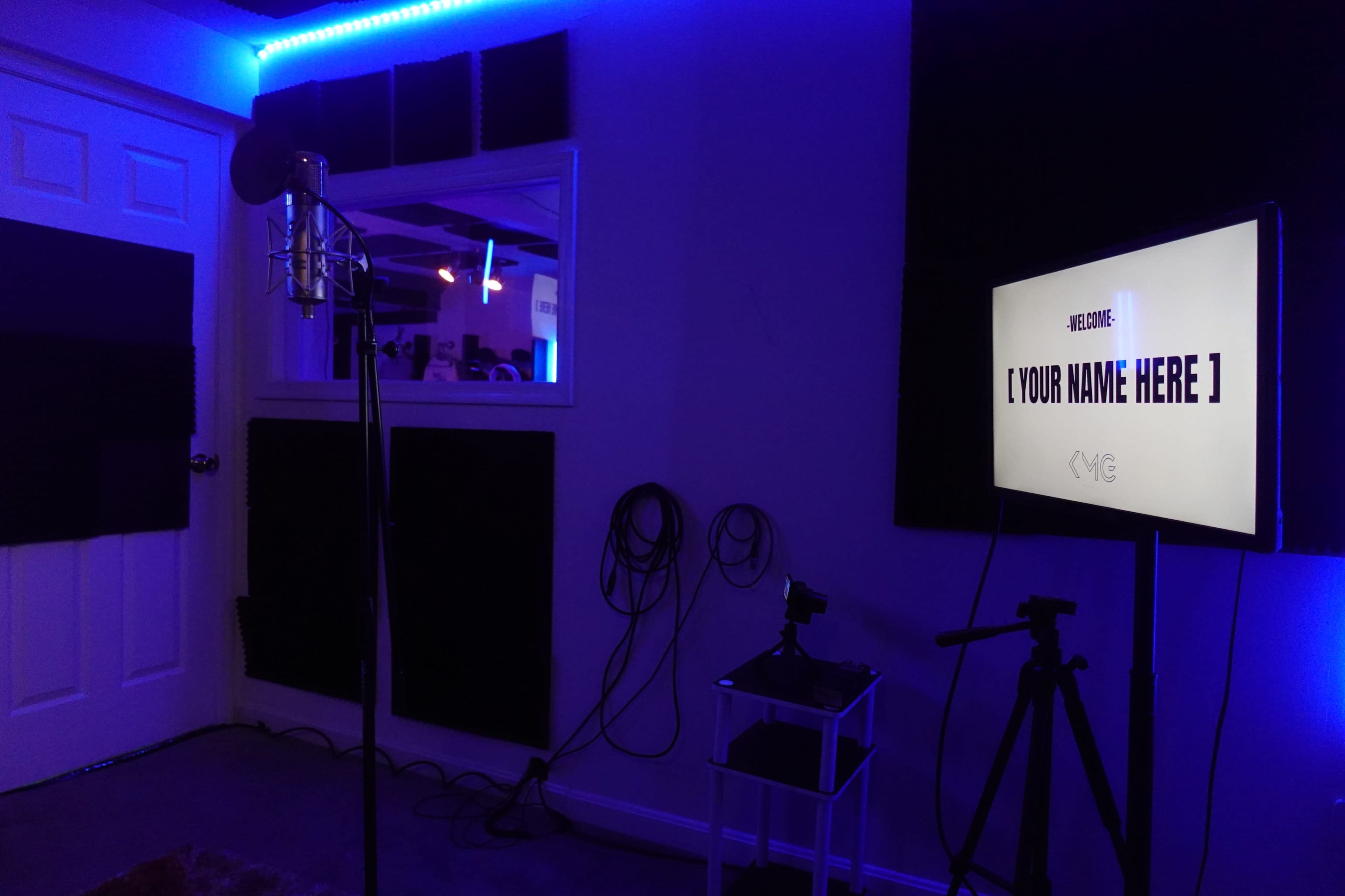 The image shows a recording studio featuring a microphone, a display screen with a placeholder for a name, and soundproofing panels on the walls, all accented by blue lighting.
