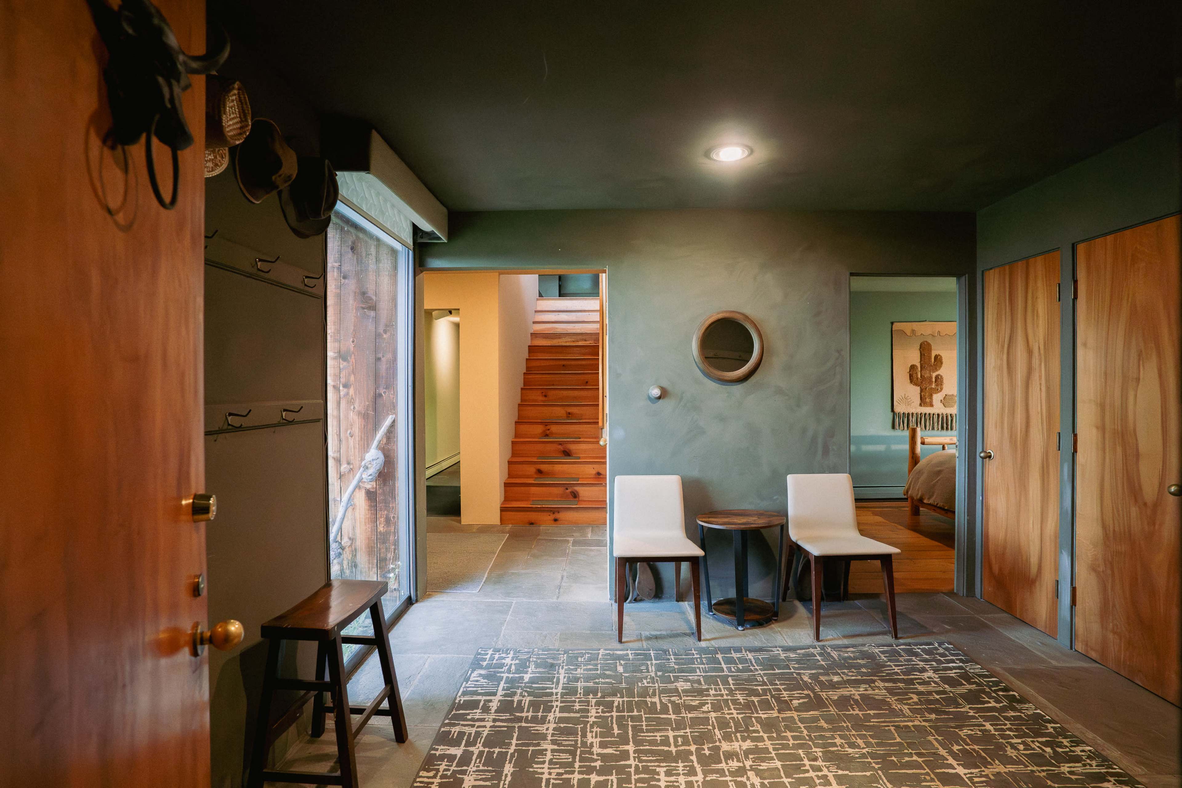 A modern entryway with a pair of chairs, a small round table, and wooden doors leading to other rooms and a staircase.