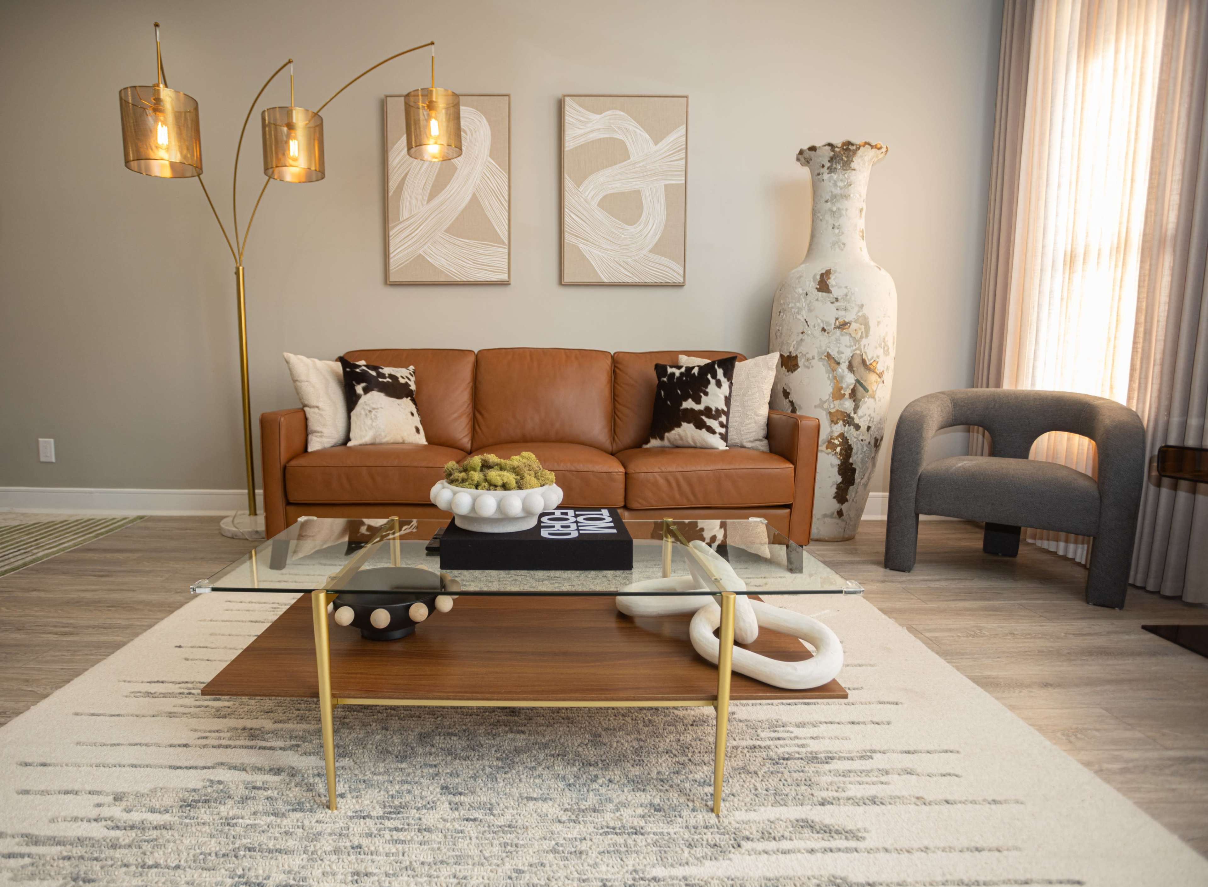 The image shows a modern living room featuring a brown leather sofa, a glass coffee table with decorative items, and a large decorative vase.