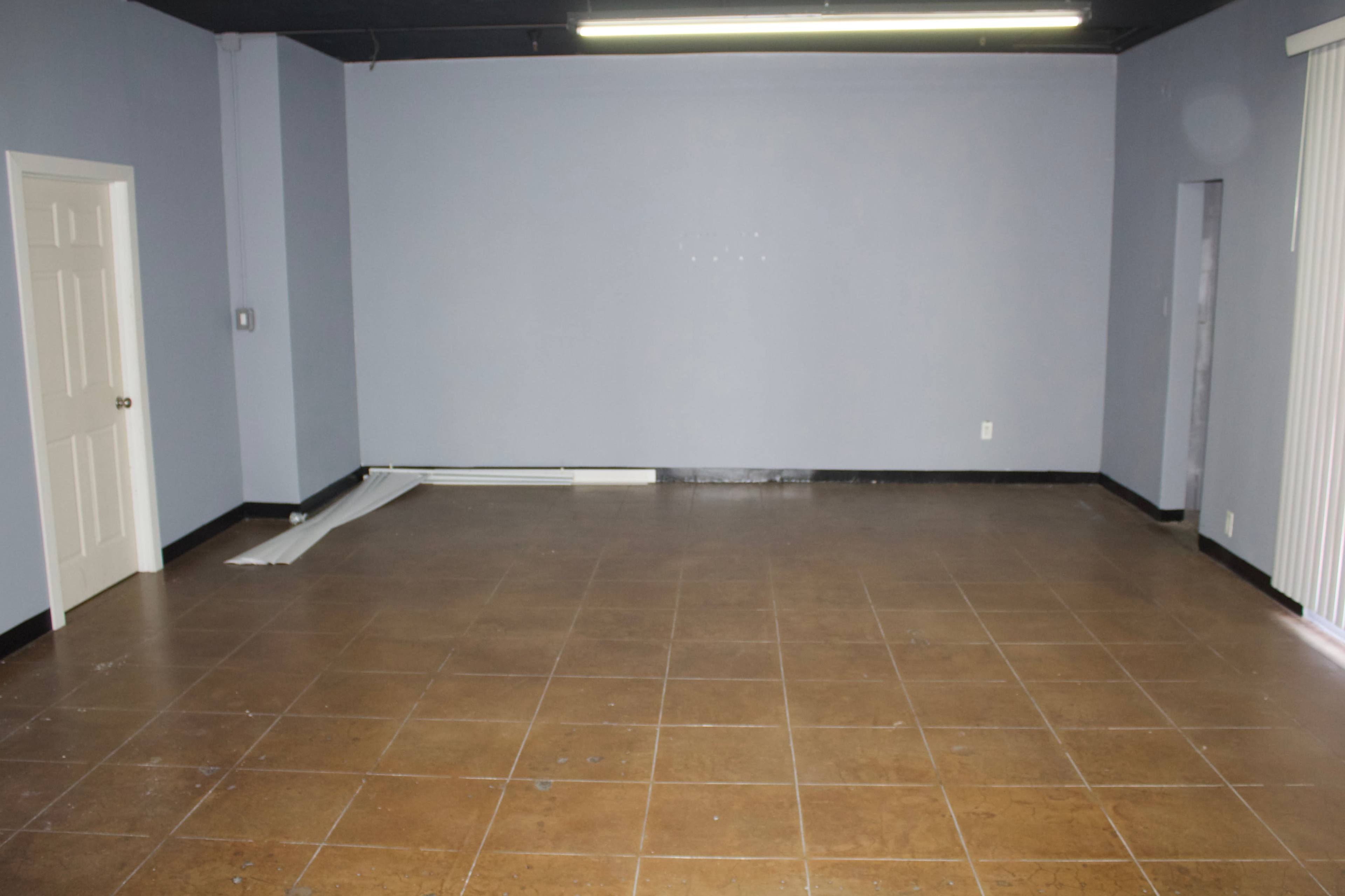 The image shows a vacant room with light blue walls, a tiled floor, and two doors on the left side.