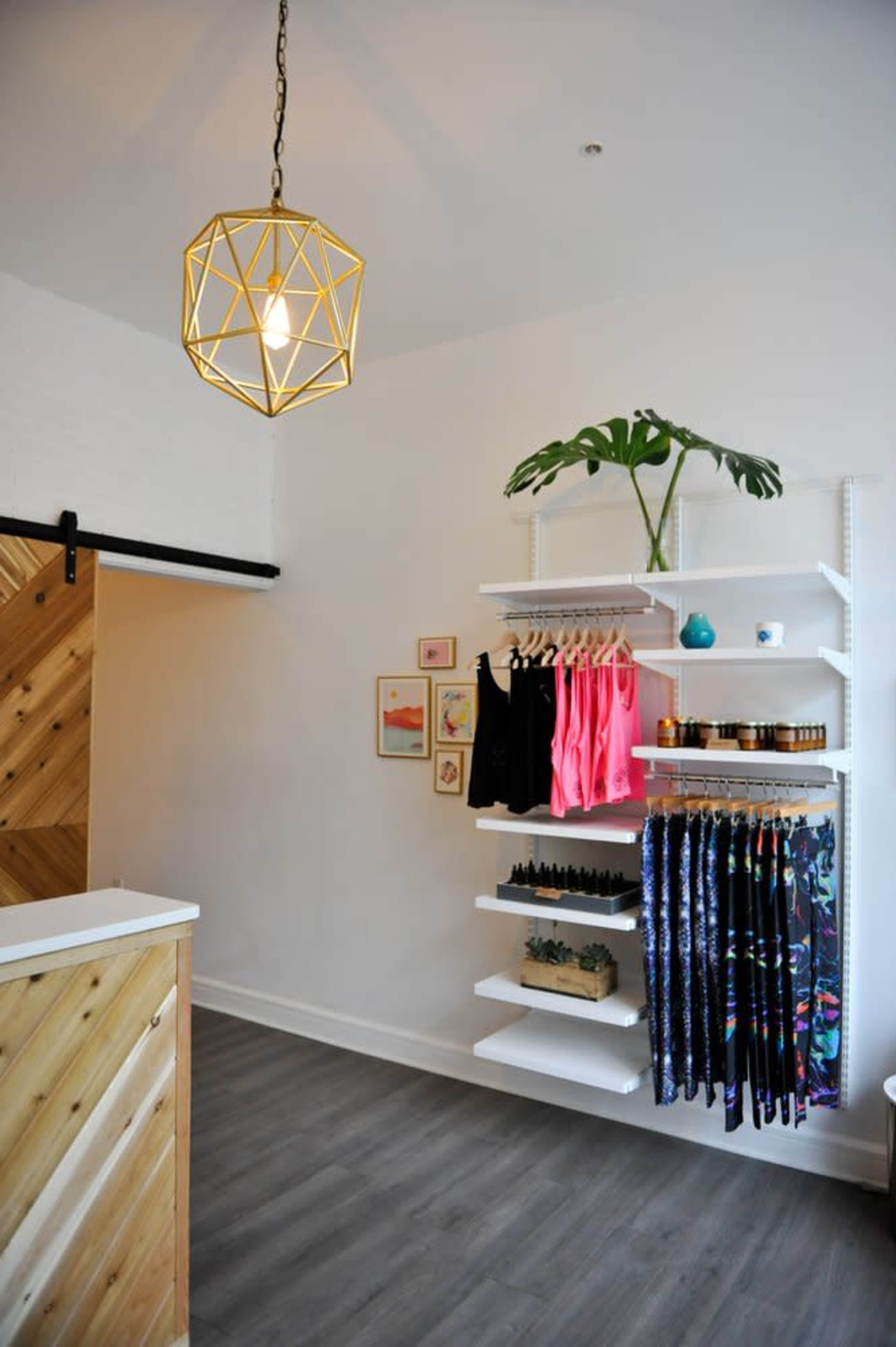 A boutique interior features a light fixture overhead, a wooden reception desk, and shelves displaying colorful clothing and products against a clean wall.
