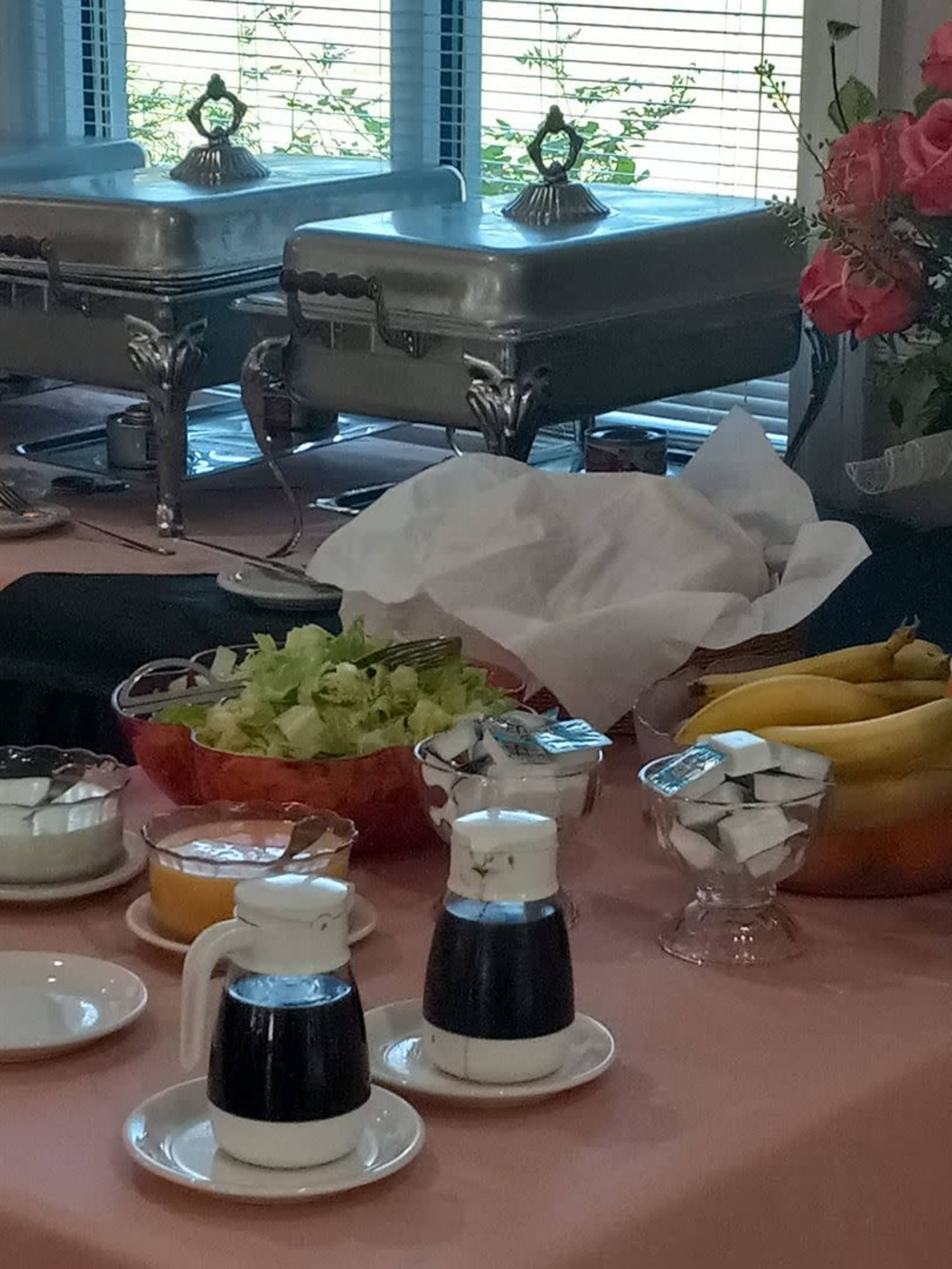 A buffet table with chafing dishes, a bowl of salad, pitchers of dark liquid, a dish of sugar cubes, and a bunch of bananas.