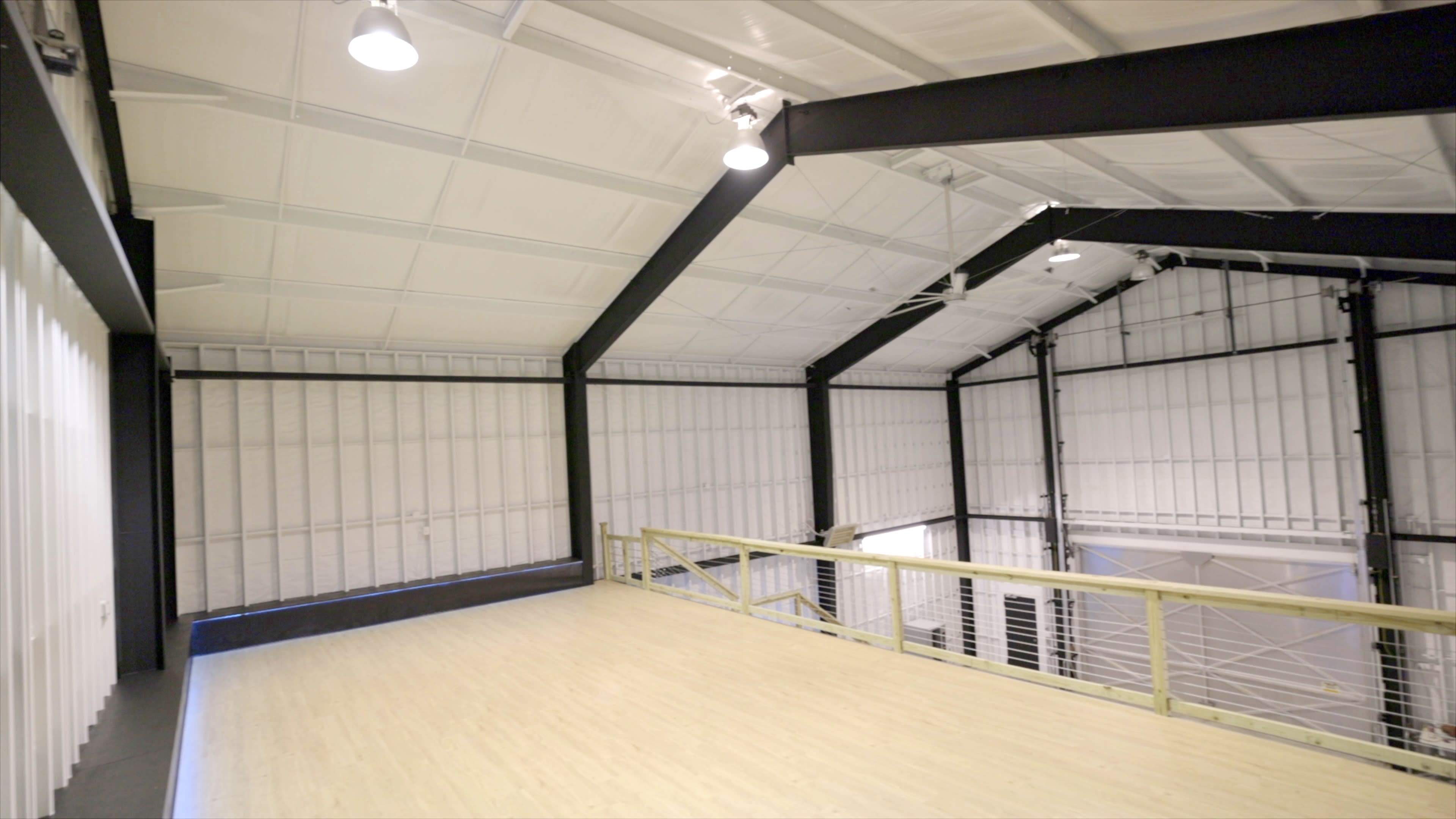 A spacious, industrial-style interior with a wooden floor and high ceilings supported by black beams.