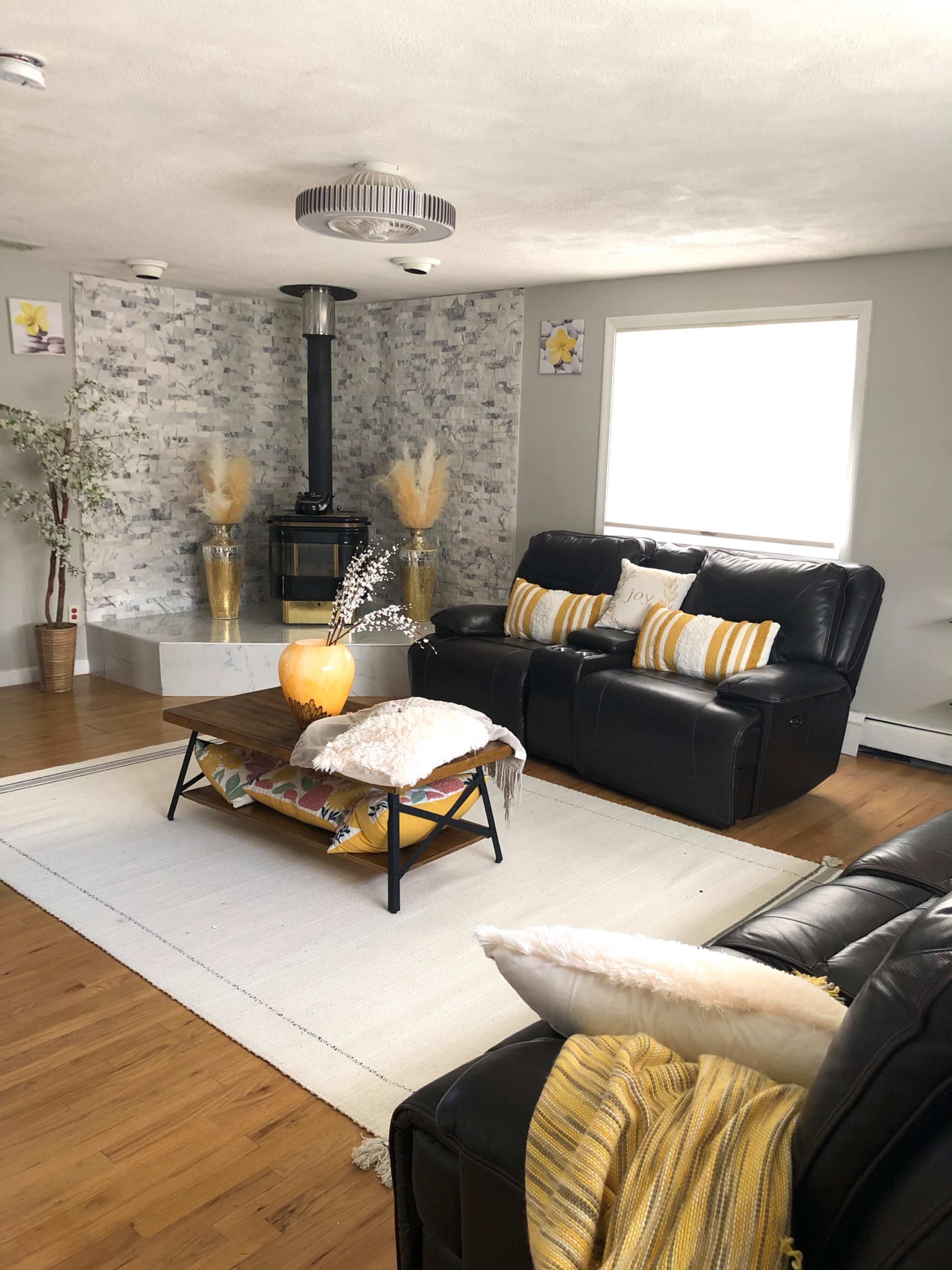 The living room features two black leather sofas facing a central coffee table, with a stone-clad fireplace in the background.