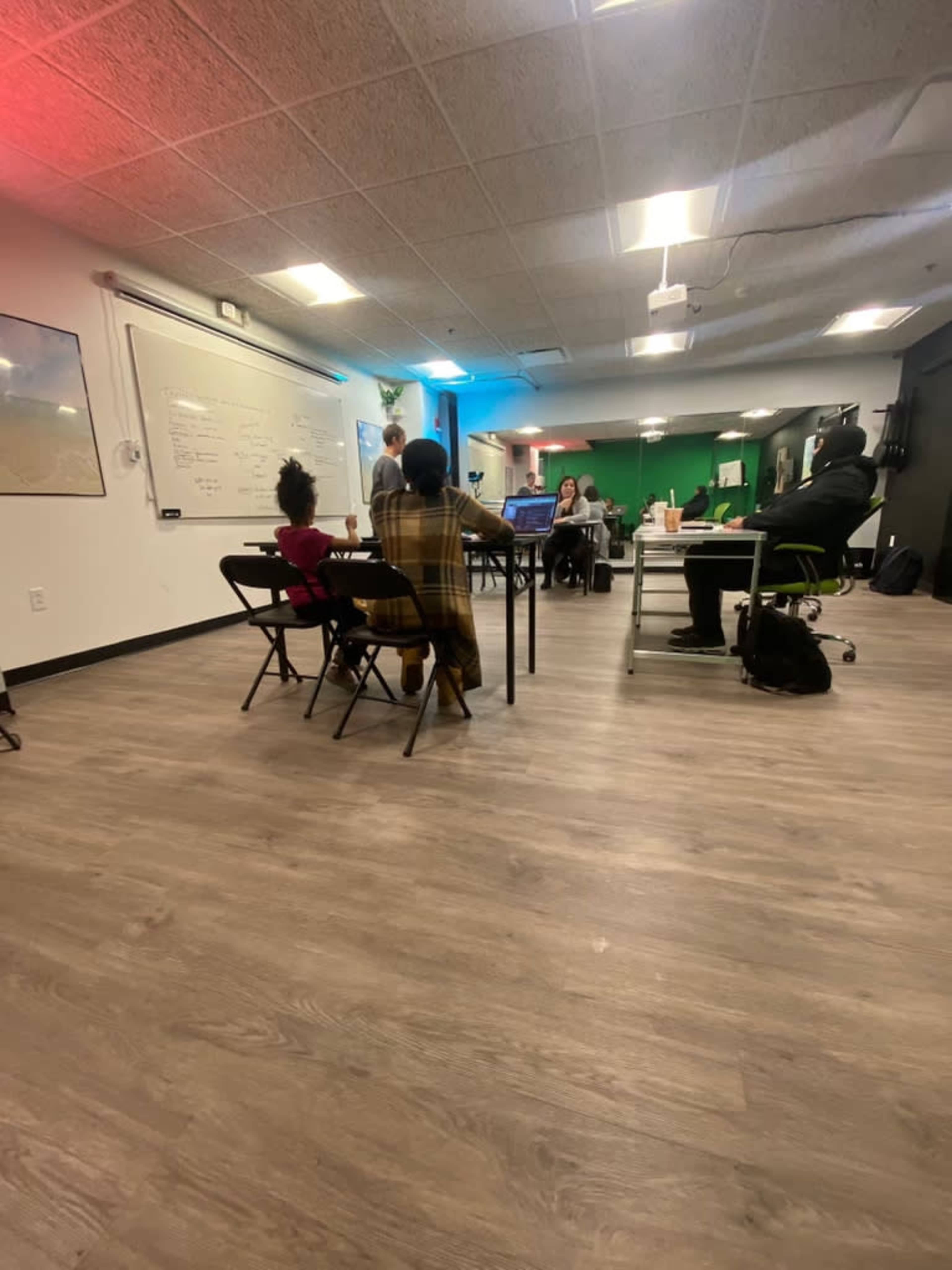 A group of people is engaged in a collaborative session in a well-lit workspace, with a child sitting at a nearby table.