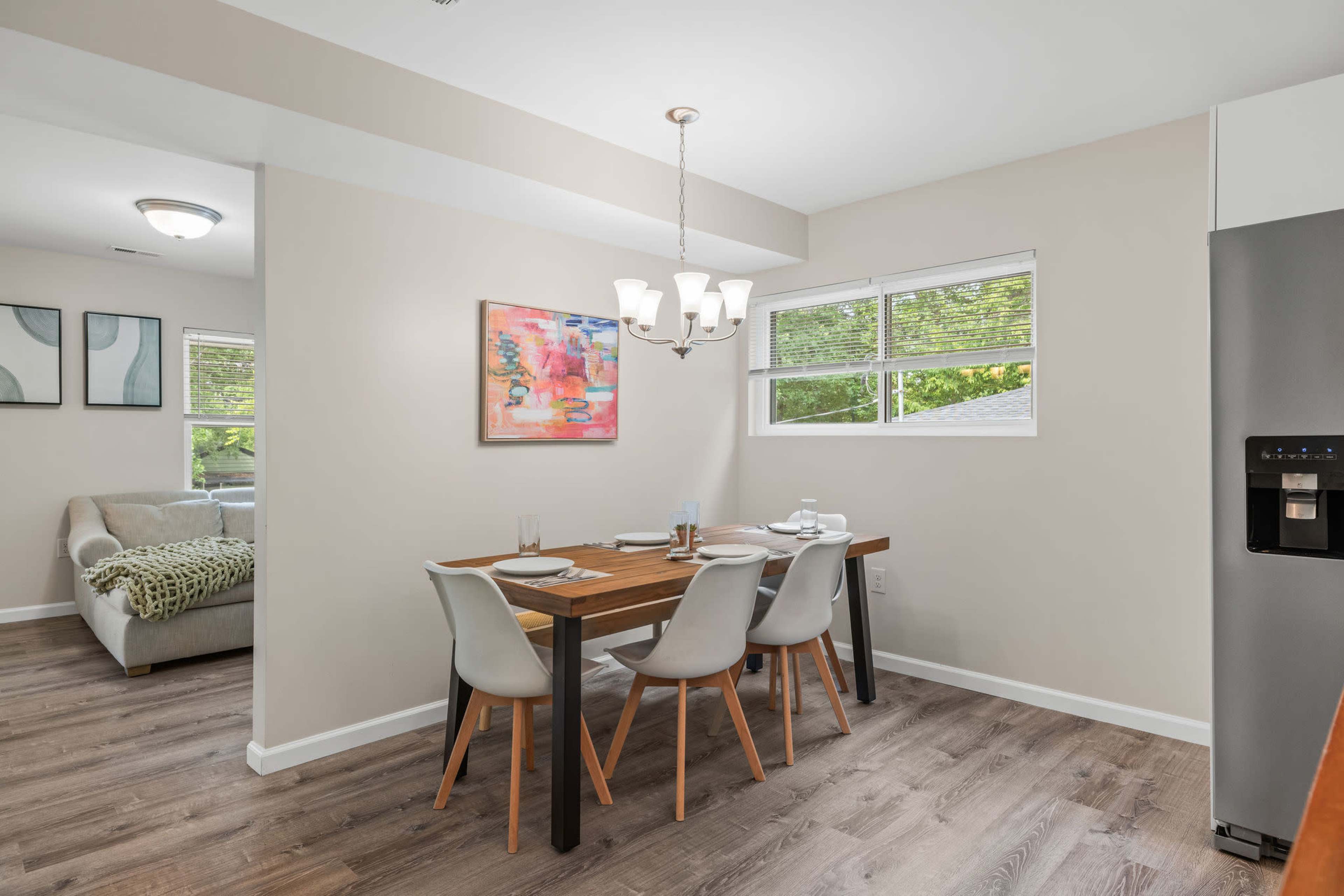 A dining area features a wooden table set for four, with modern chairs and a colorful abstract painting on the wall.