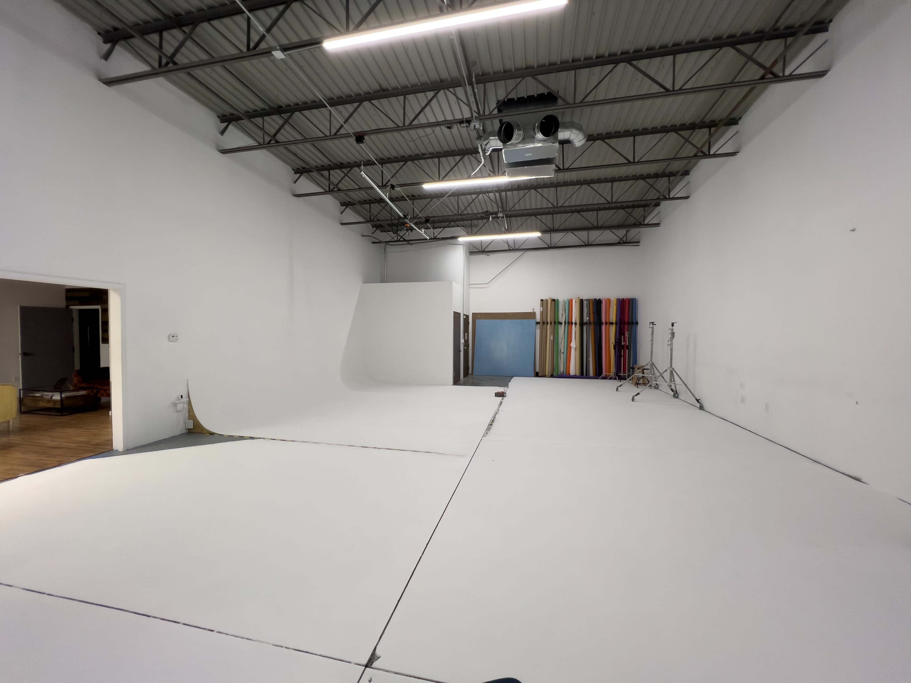 A spacious photography studio with a smooth white floor, white walls, and a backdrop stand with multiple colored backdrops.