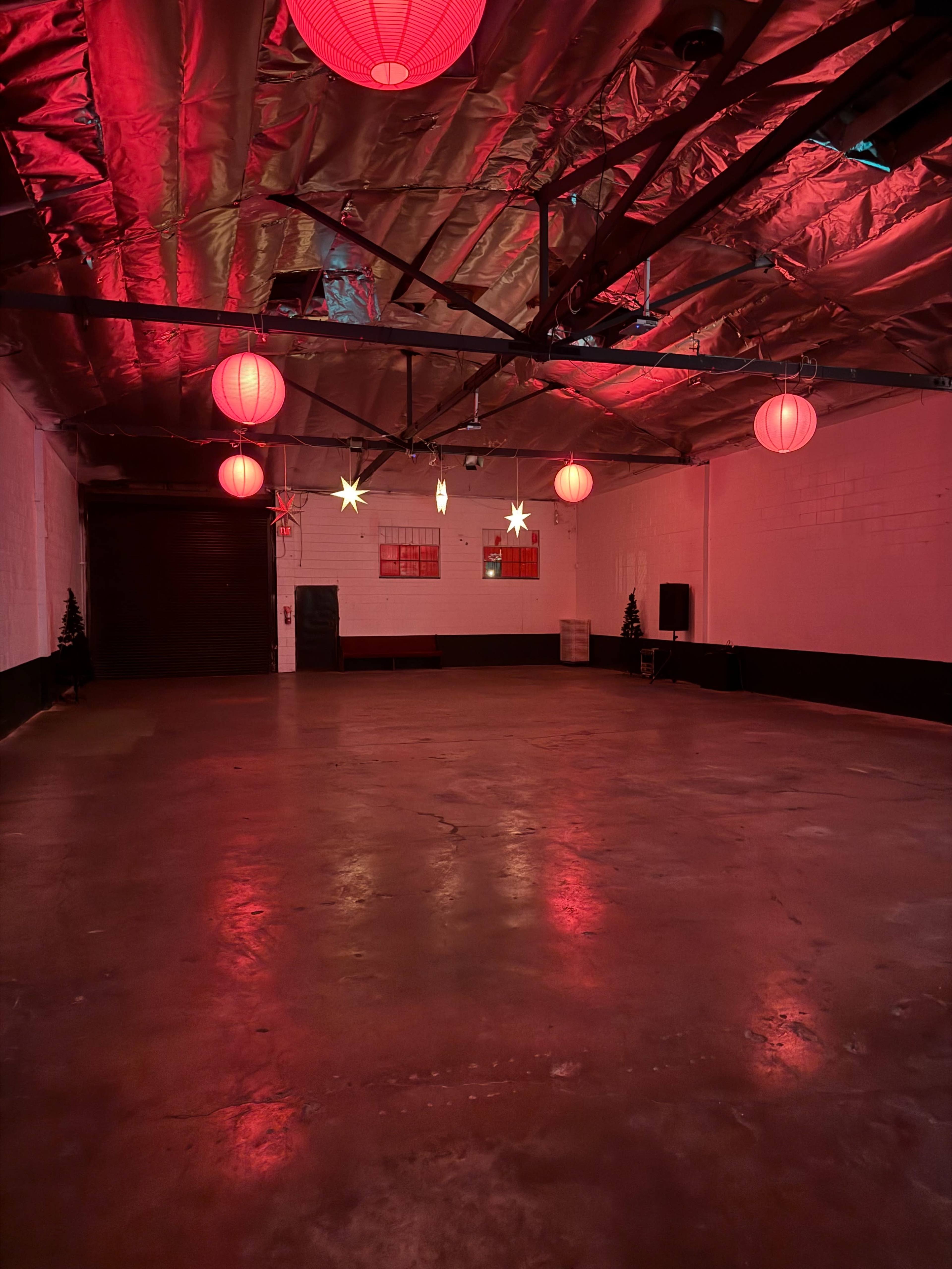 The image shows an empty warehouse space with a polished concrete floor, red lanterns hanging from the ceiling, and decorative stars attached to the walls, illuminated by red lighting.