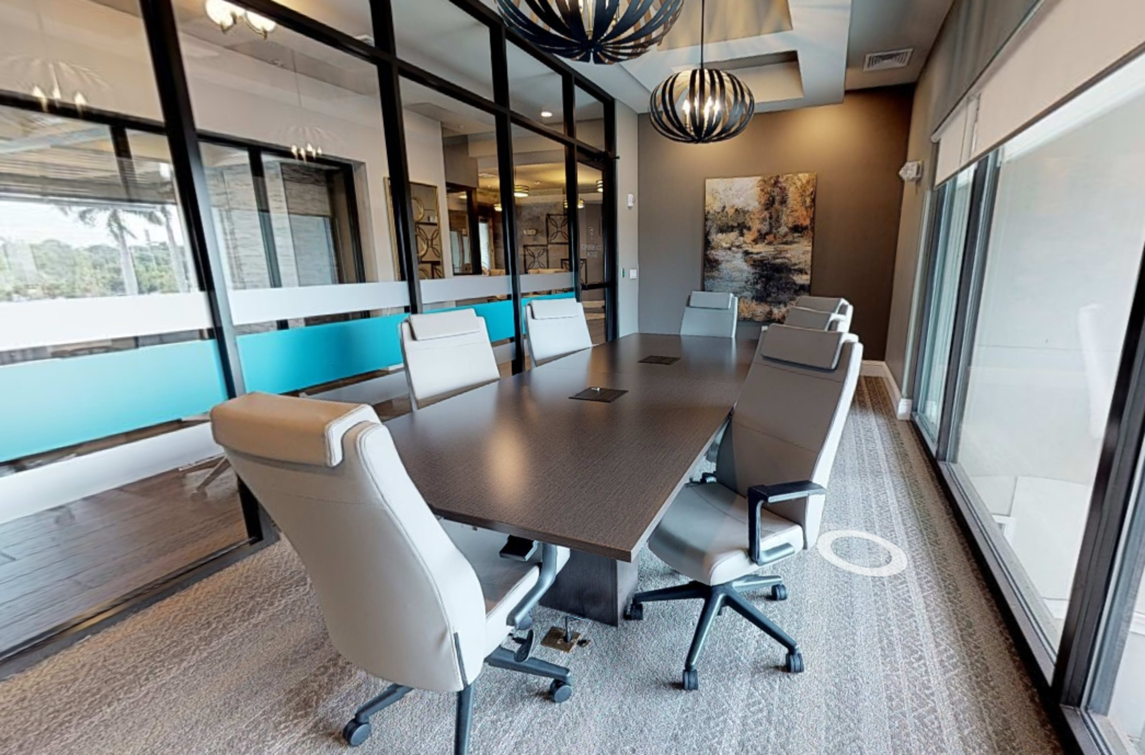 A modern conference room features a long table surrounded by ergonomic chairs and large windows with views to the outside.