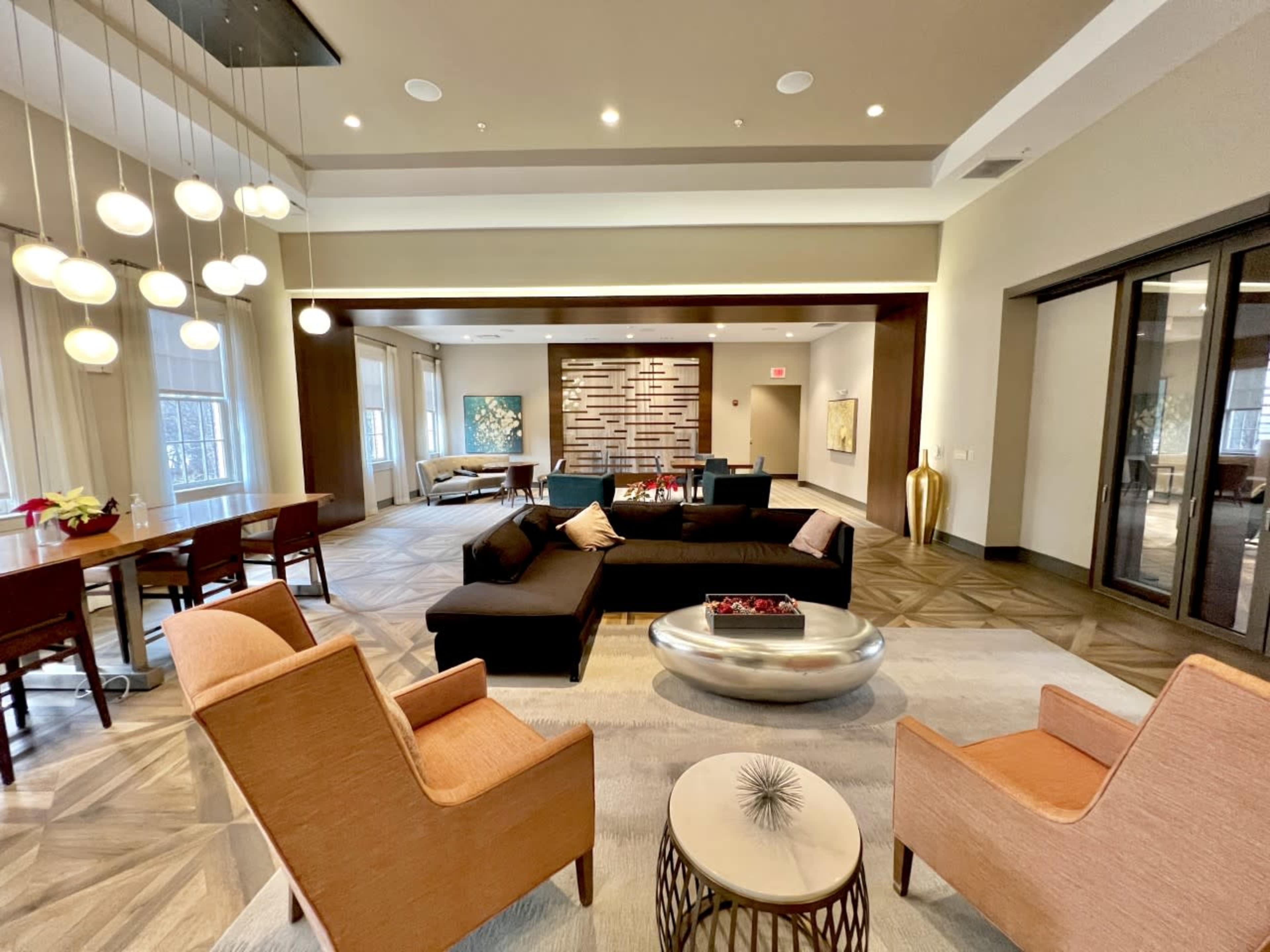 A modern living area features a sectional sofa, two armchairs, and a coffee table, surrounded by decorative art and a dining space in the background.