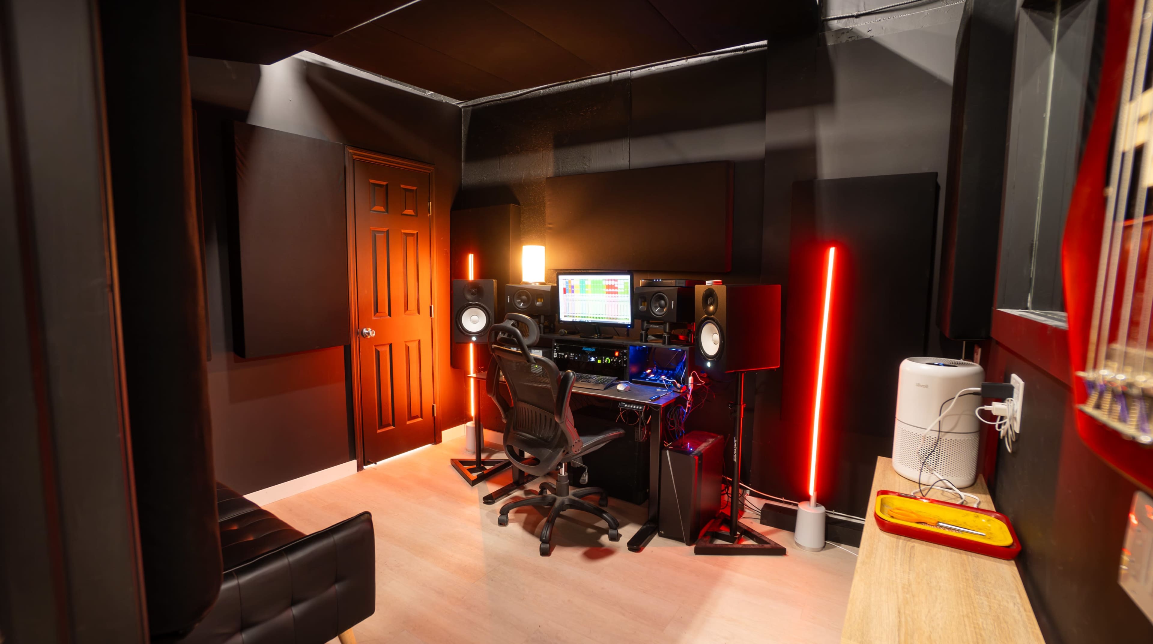 The image shows a modern music studio with a keyboard, monitors, and ambient lighting, featuring a dark color scheme and soundproofing panels on the walls.