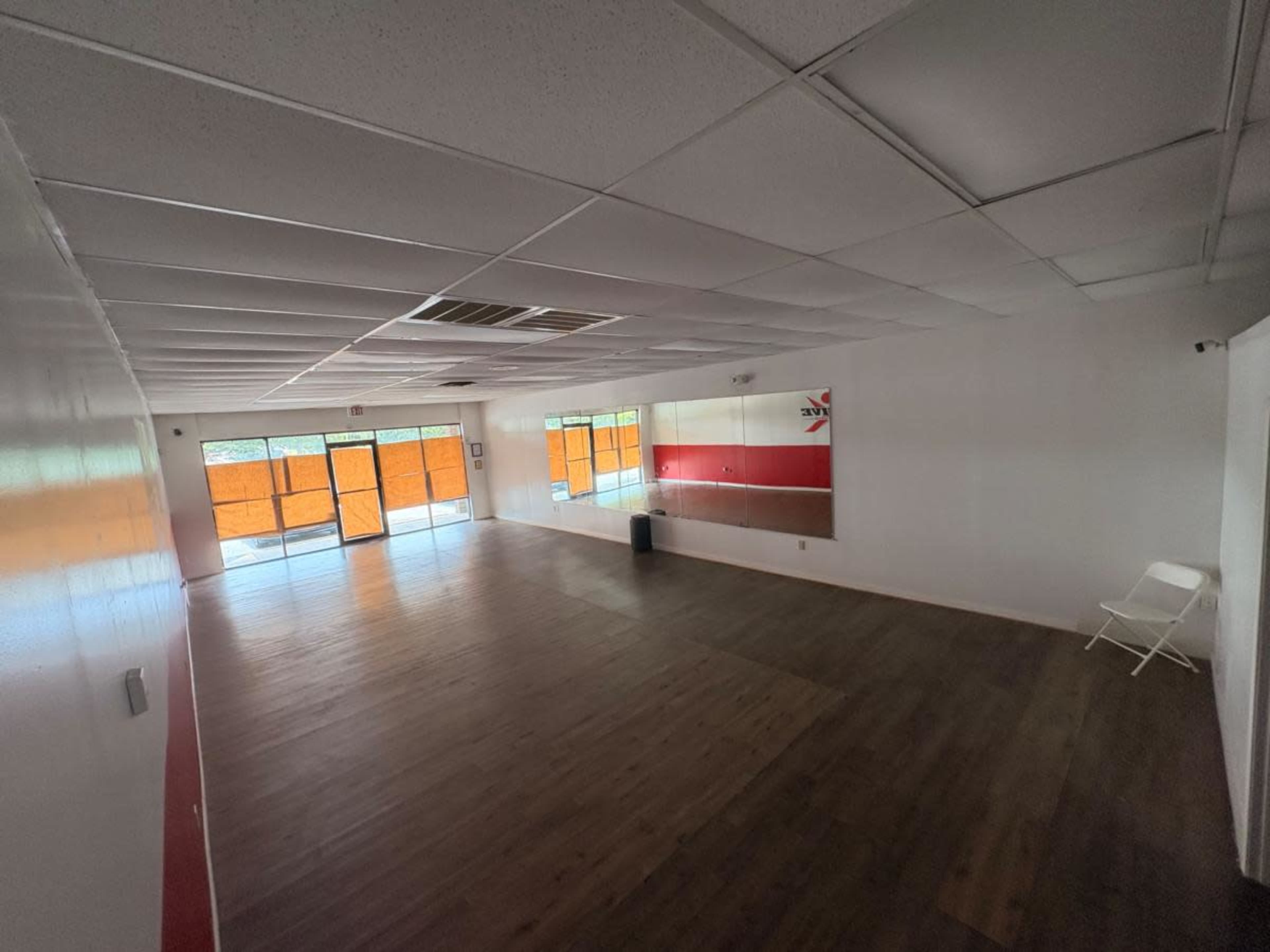 The image shows an empty room with wooden flooring, white walls, and large windows covered by orange blinds.