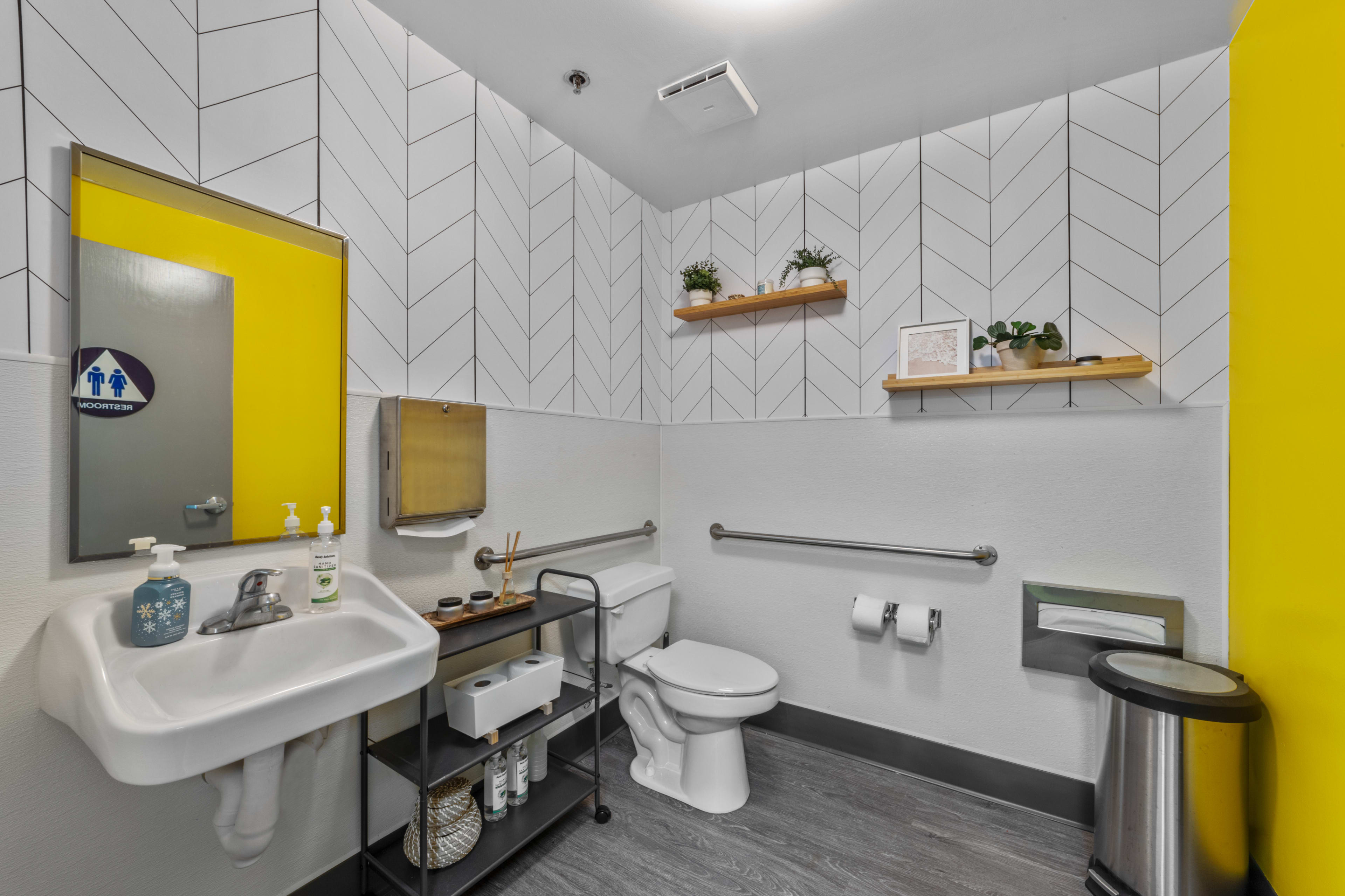 A modern restroom featuring a white toilet, a wall-mounted sink, and yellow accent walls with decorative shelves.