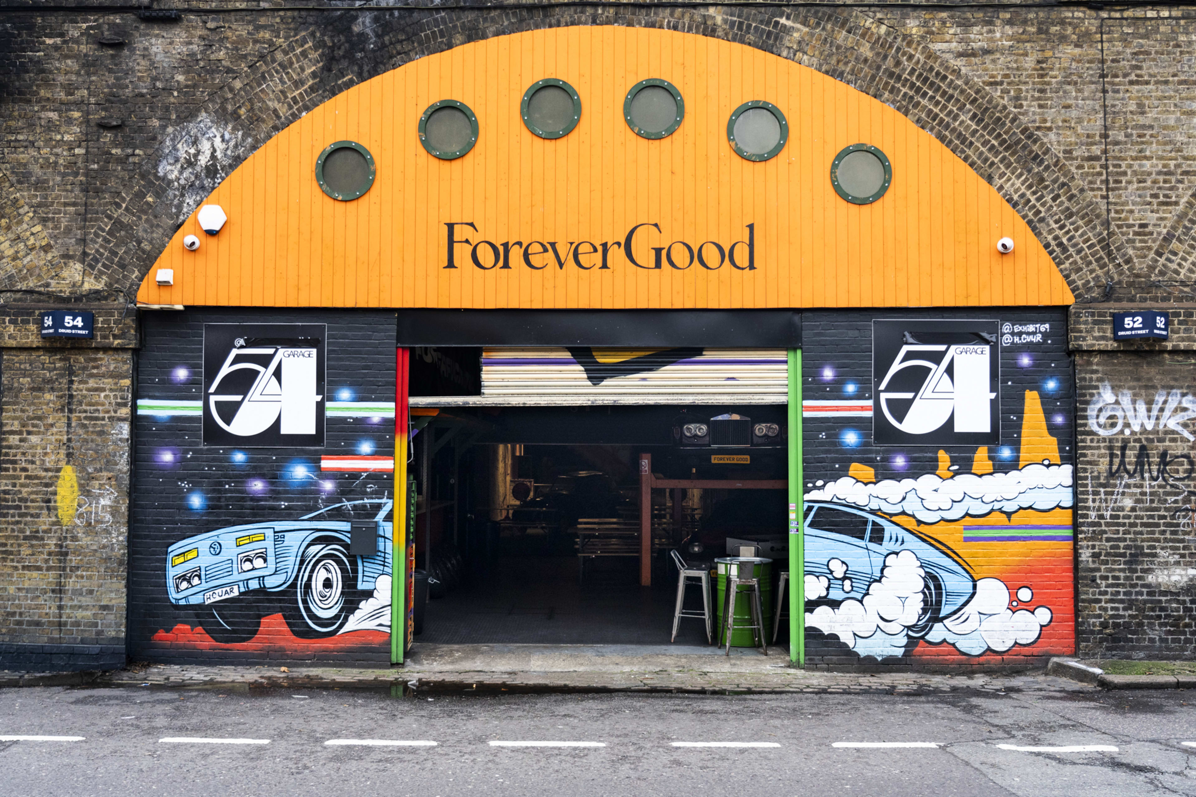 The image shows a vivid mural of a classic car in front of a garage with the words "Forever Good" and a colorful design above the entrance.