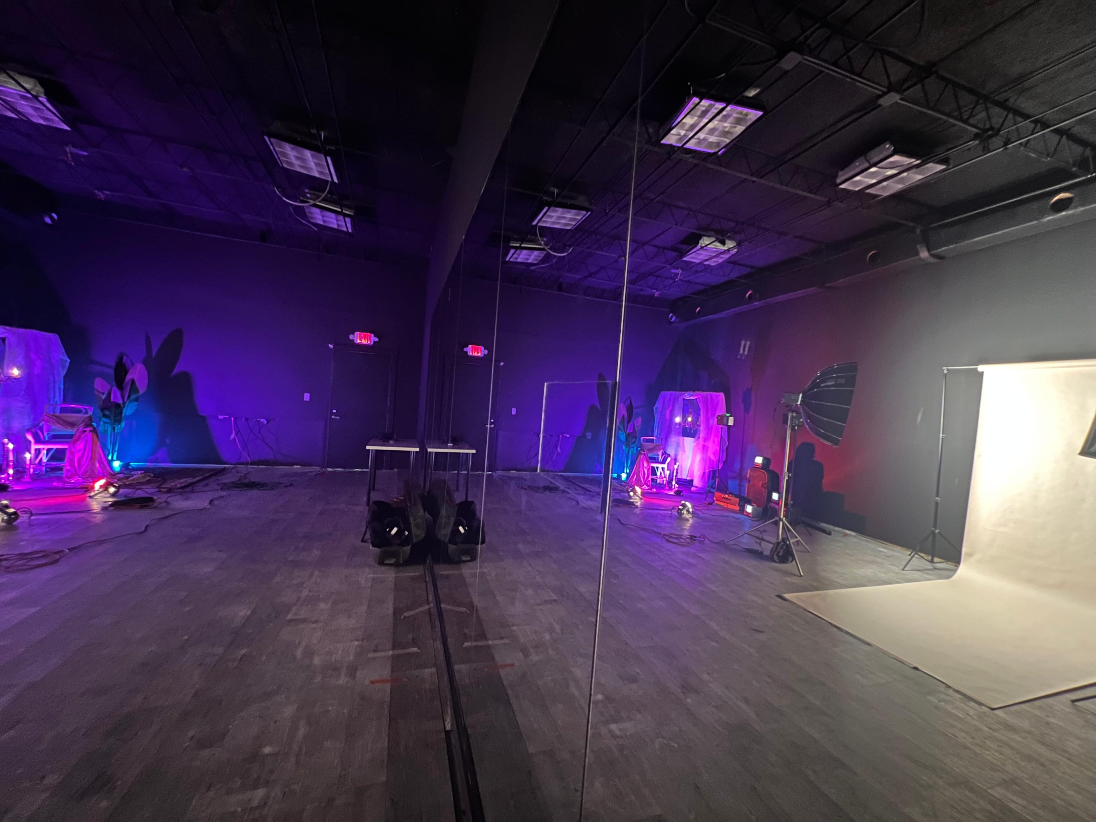 The image shows a dimly lit studio space with multiple lighting setups, including a backdrop and photography equipment, surrounded by mirrors.