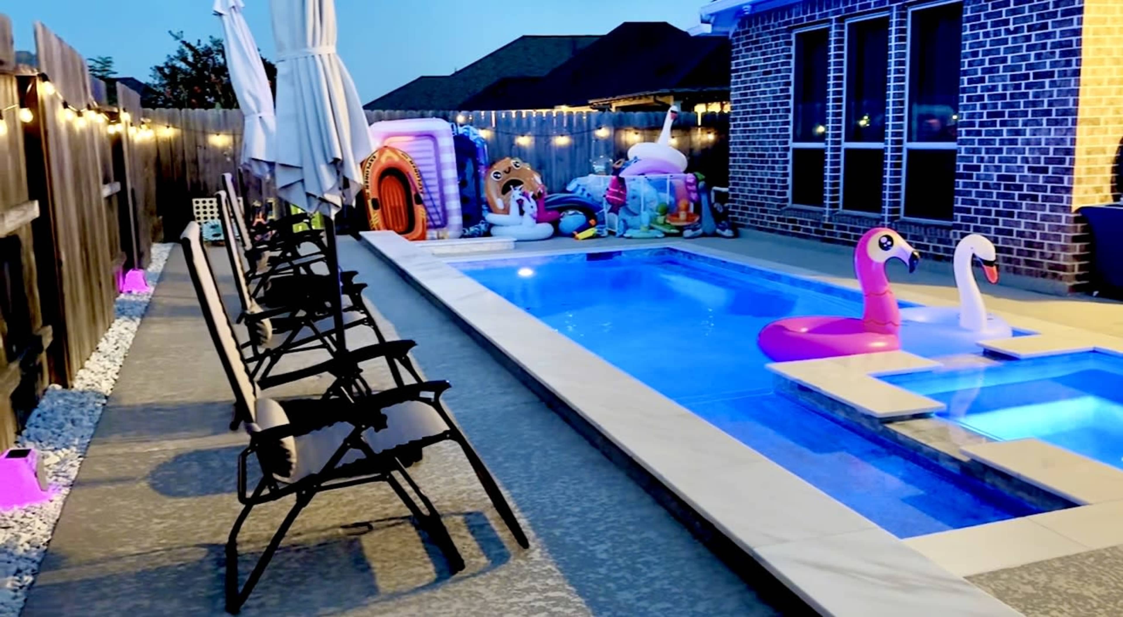 The scene features a backyard pool area with a lighted pool, inflatable toys, and several chairs arranged along the edge.