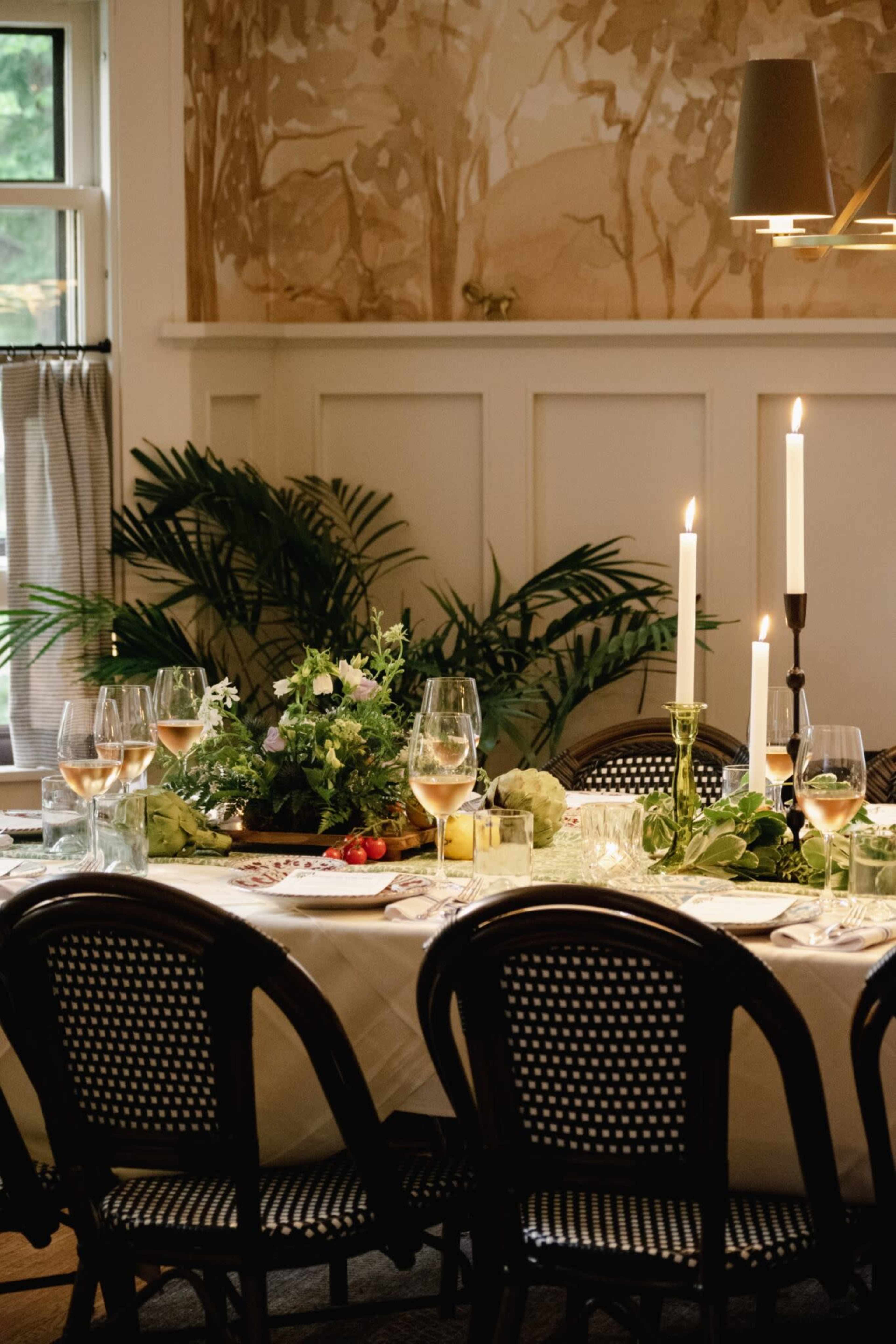 A dining table is set with elegant glassware and candles, surrounded by chairs and adorned with a floral centerpiece.