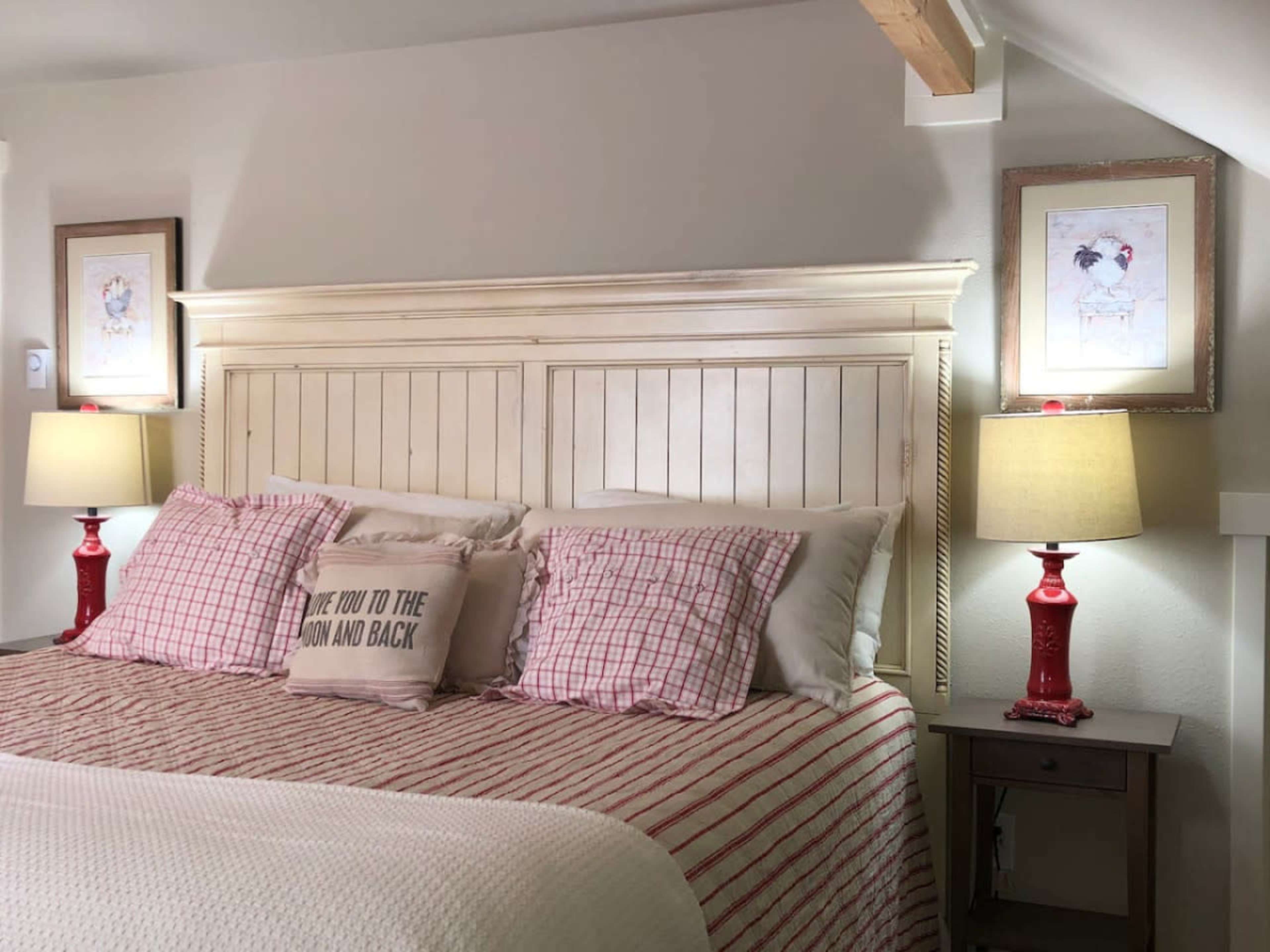 The image shows a cozy bedroom with a wooden headboard, red and white checked pillows, and lamps on either side of the bed.