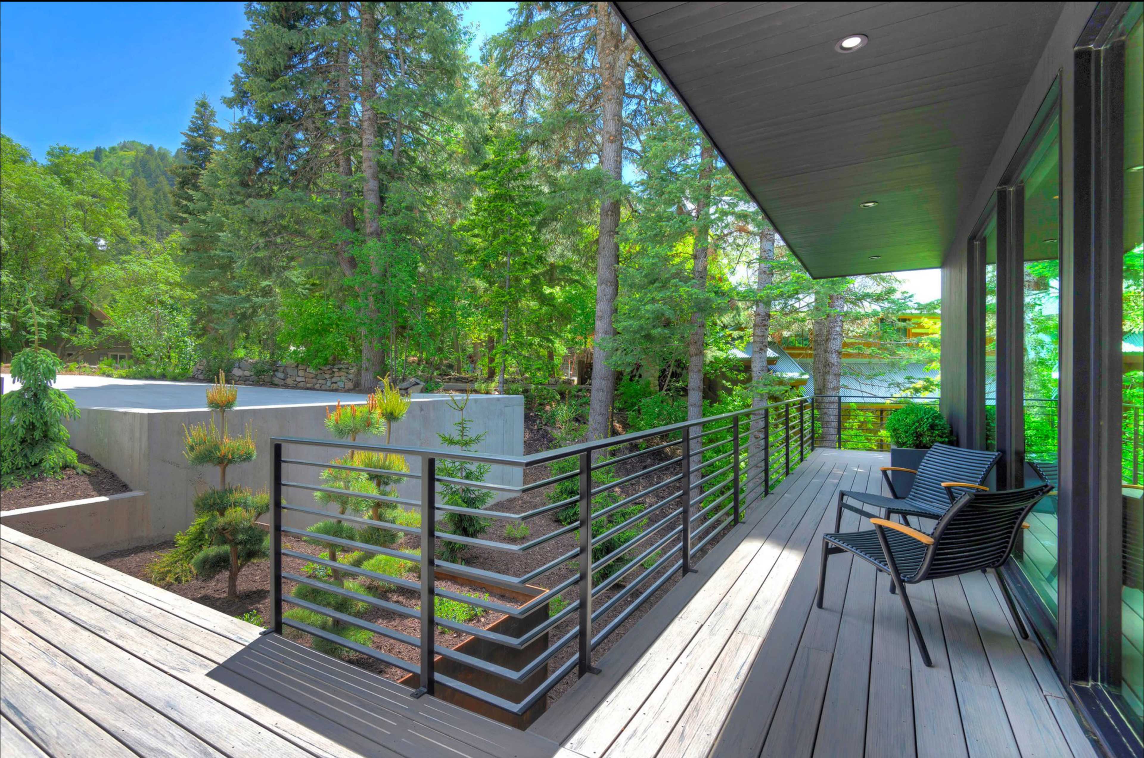 A modern balcony with a railing overlooks a landscaped area surrounded by trees.