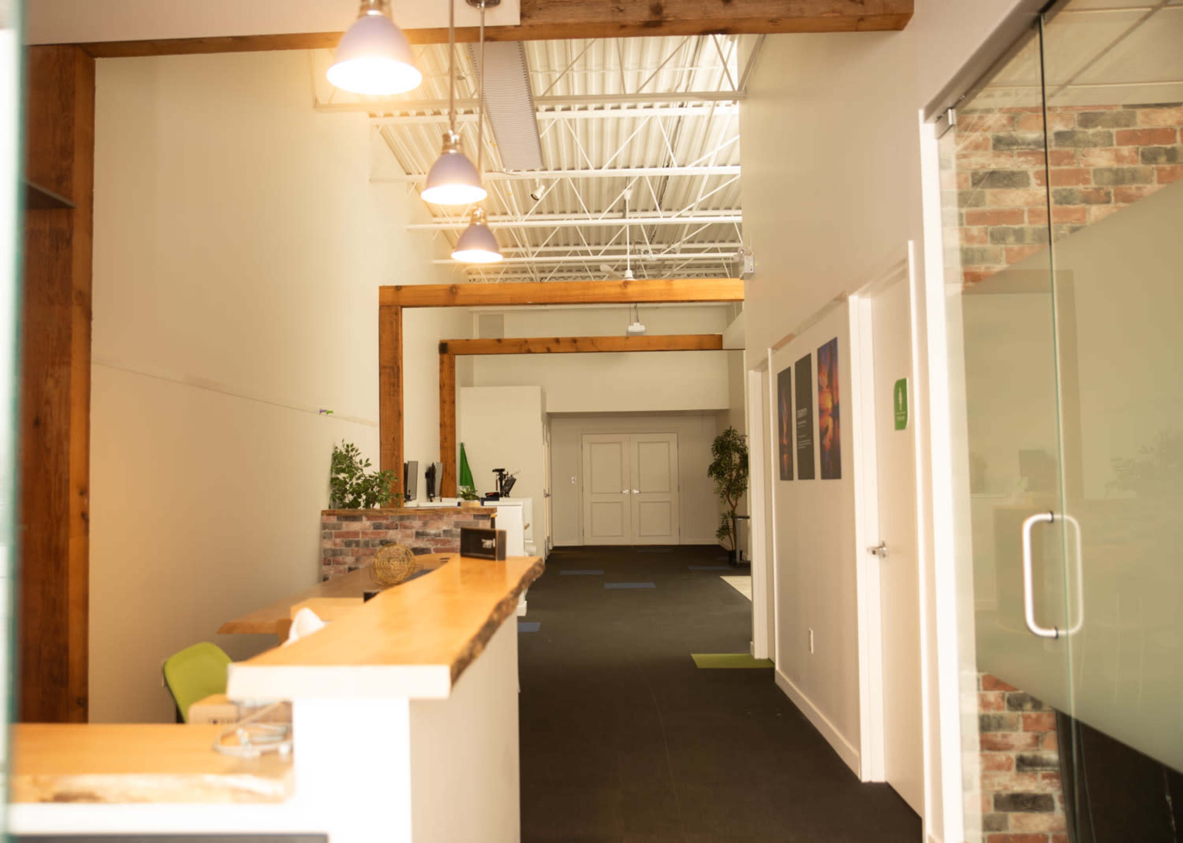 A modern office interior featuring a reception area with wooden beams, a front desk, and rooms off a hallway.