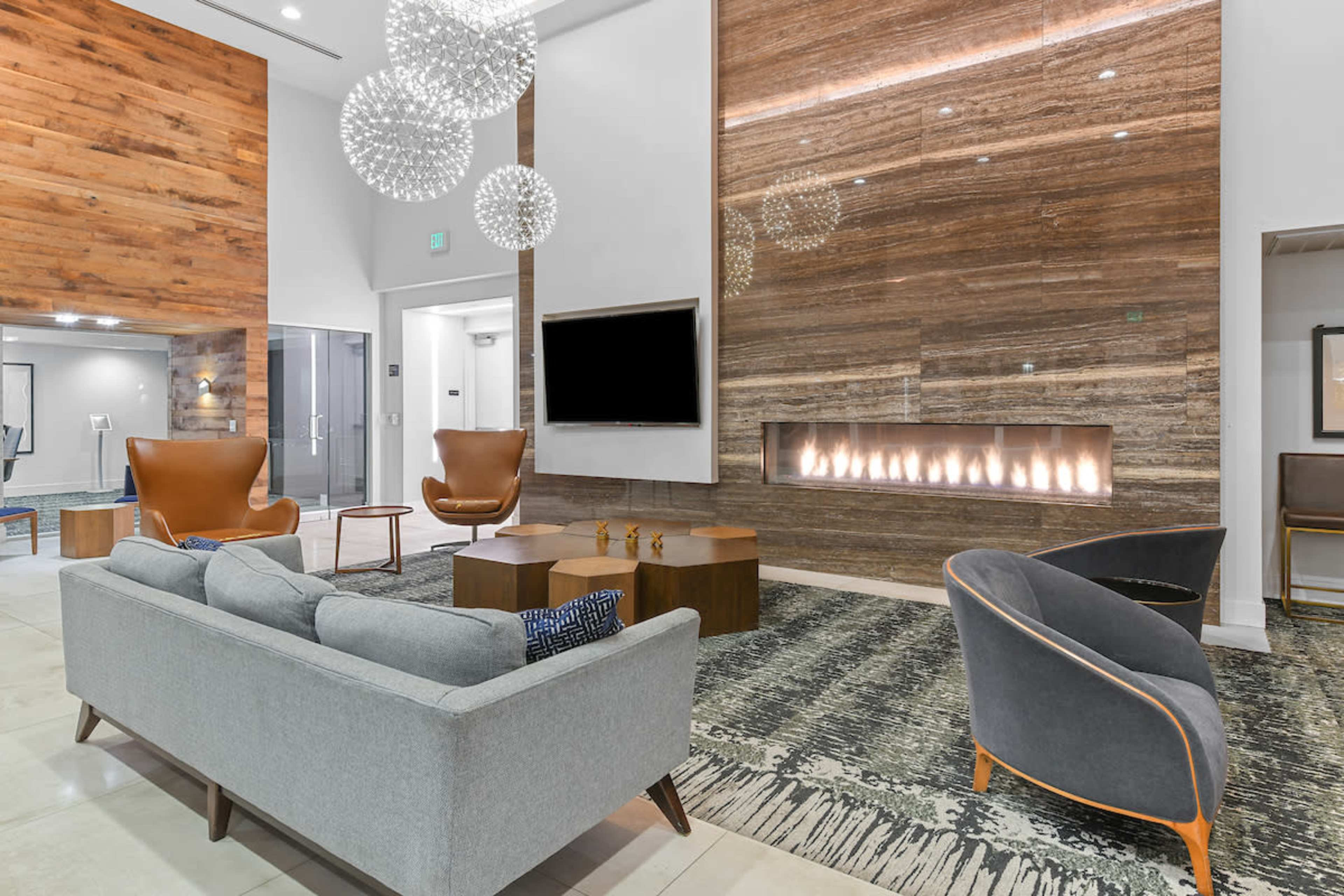A modern lobby area with a large stone wall, a linear fireplace, stylish seating, and decorative light fixtures.
