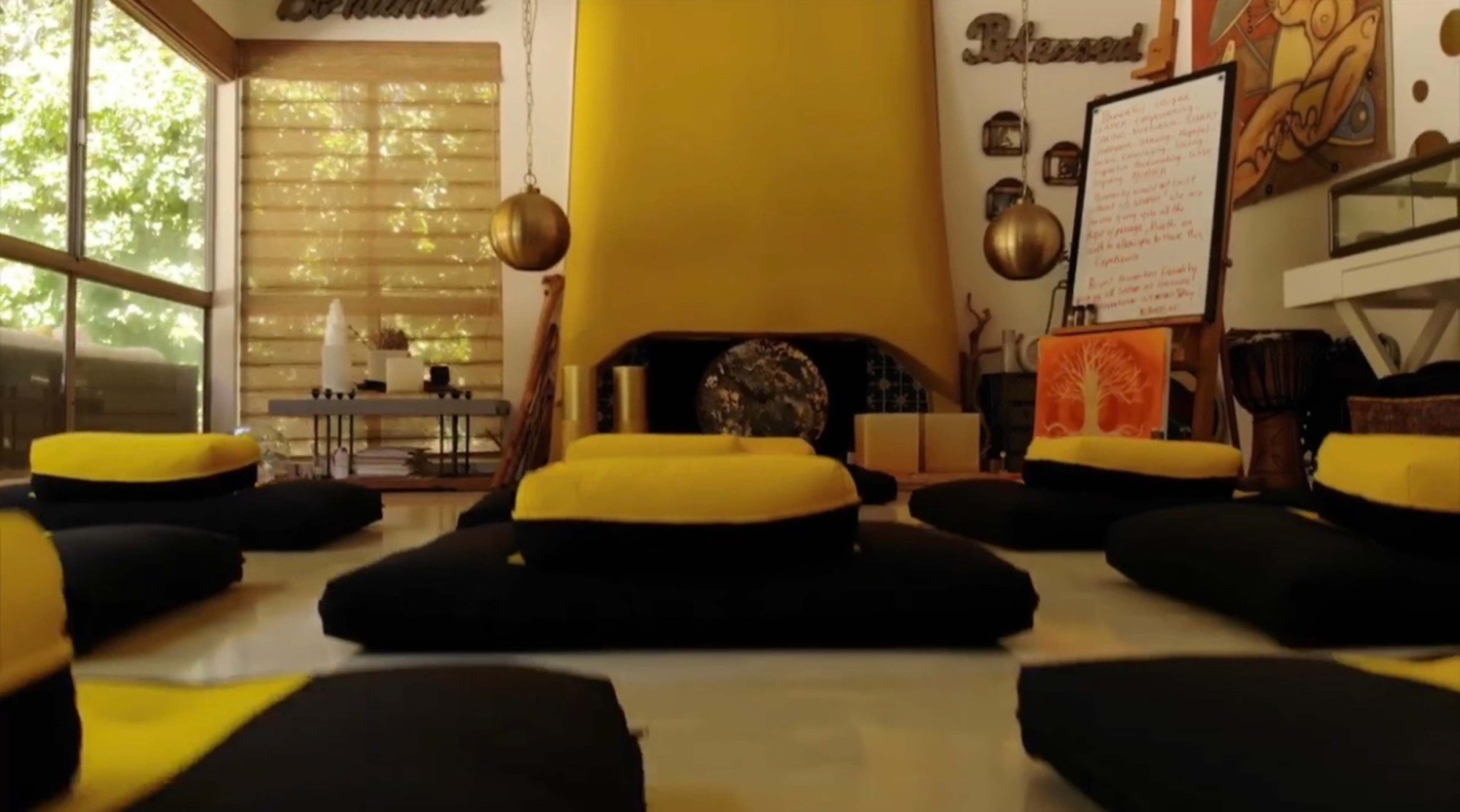 A room set up for meditation, with several yellow and black cushions arranged on the floor, a yellow wall, and a whiteboard nearby.