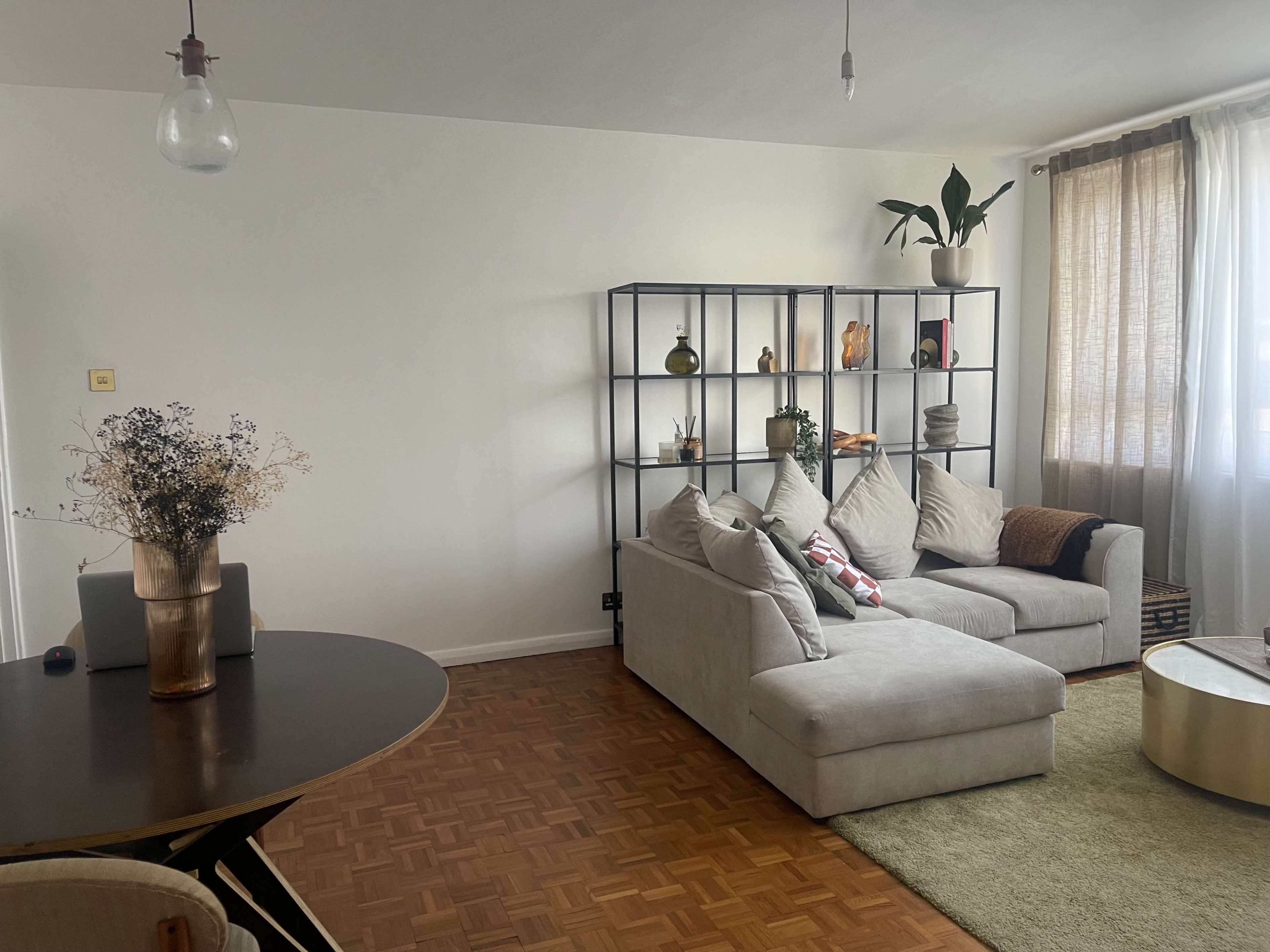 A modern living room featuring a light gray sectional sofa, a bookshelf with decorative items, and a circular dining table.