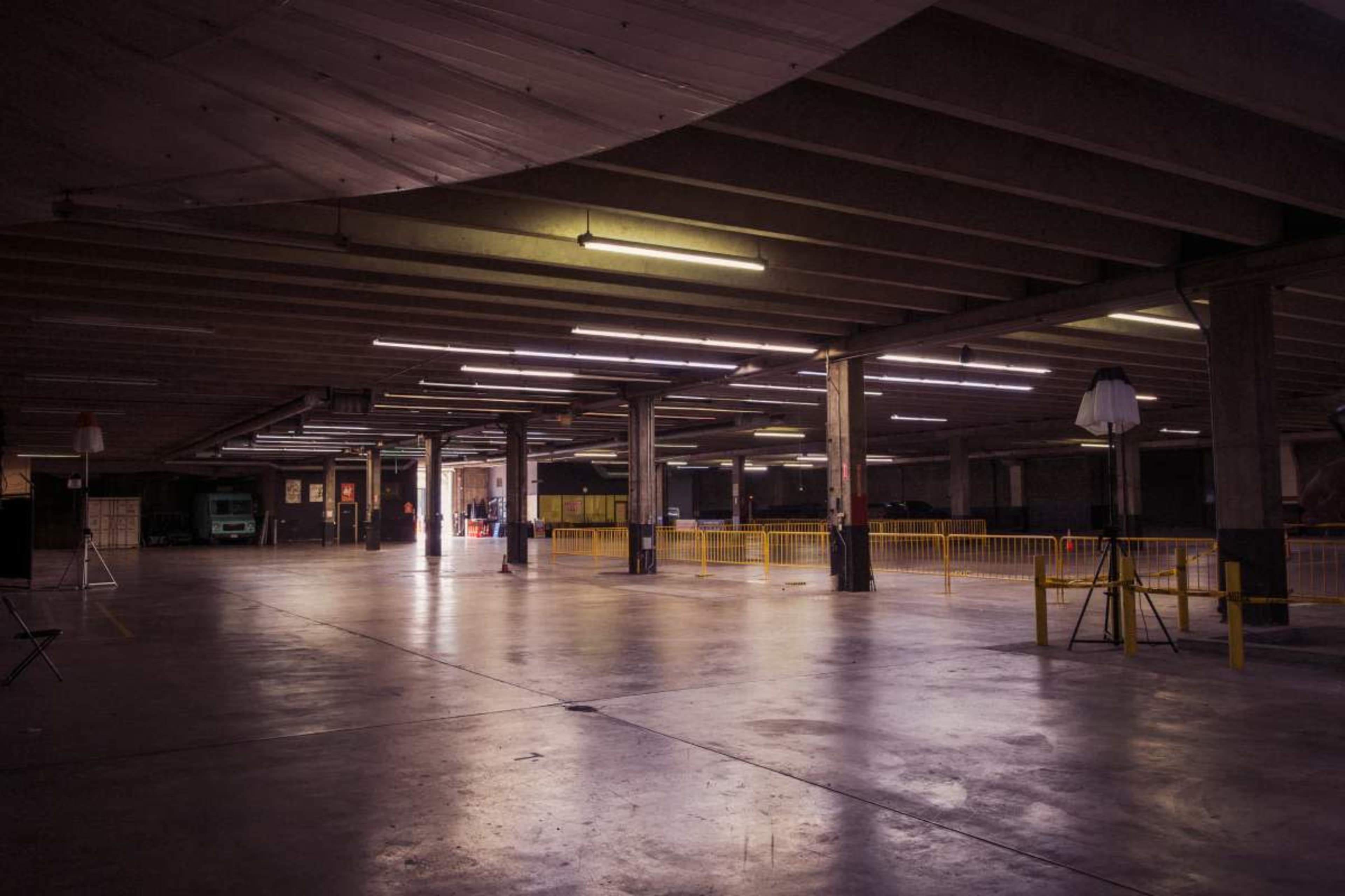 The image shows an empty underground parking garage with fluorescent lighting and yellow barriers spaced throughout the area.