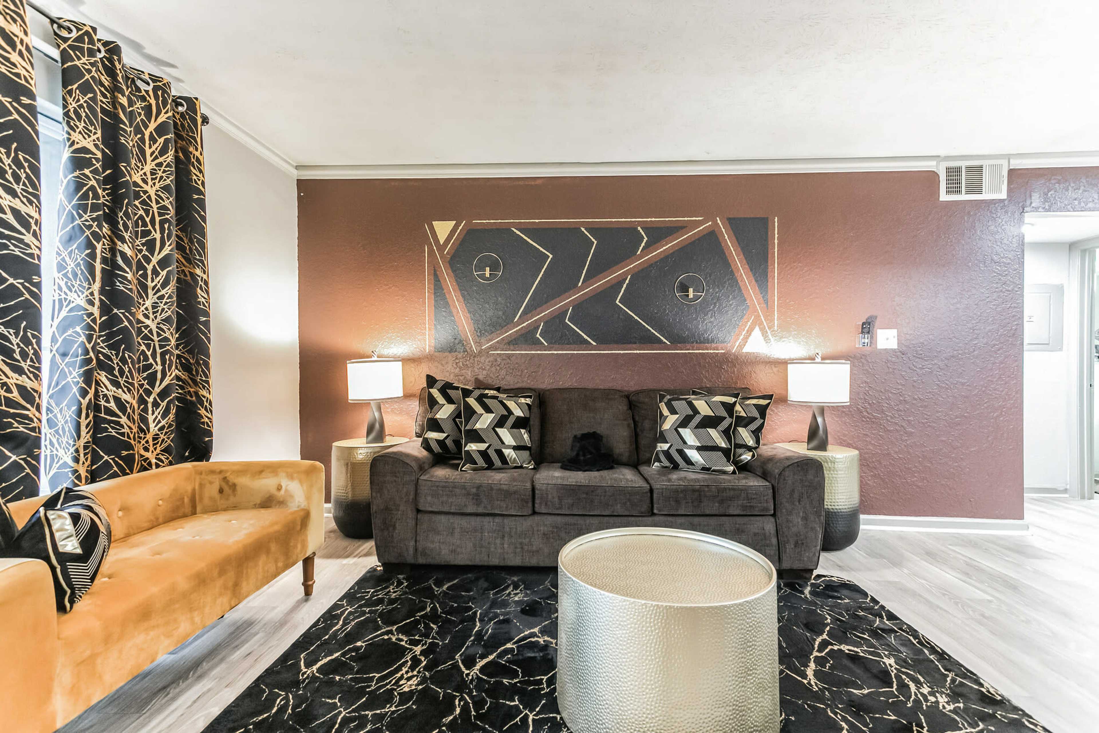 A living room with a dark sofa, a gold-colored coffee table, and decorative curtains featuring a tree branch pattern.
