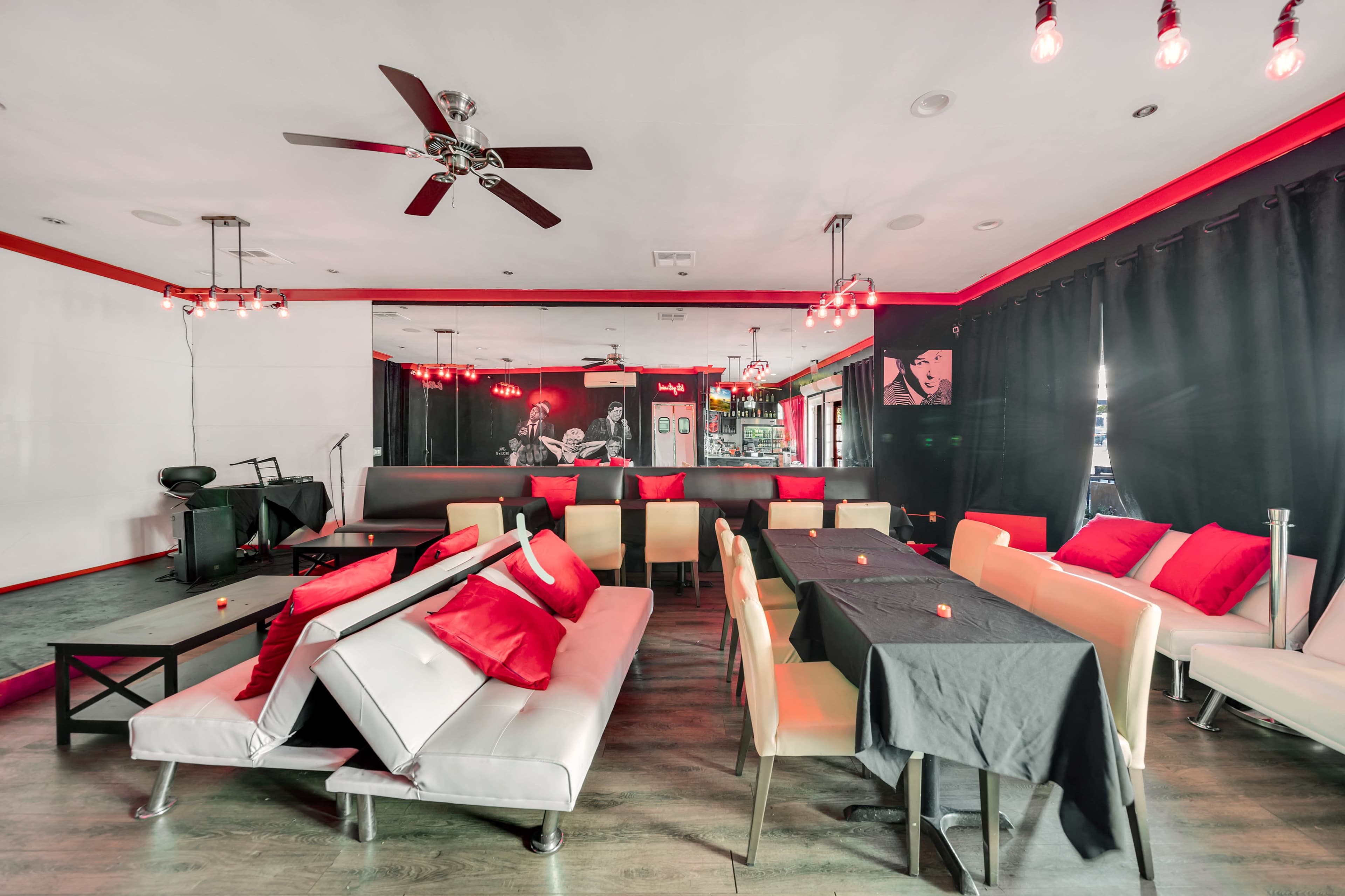 A modern cafe interior with a mix of white and black furniture, red accents, and dim lighting from hanging light fixtures.