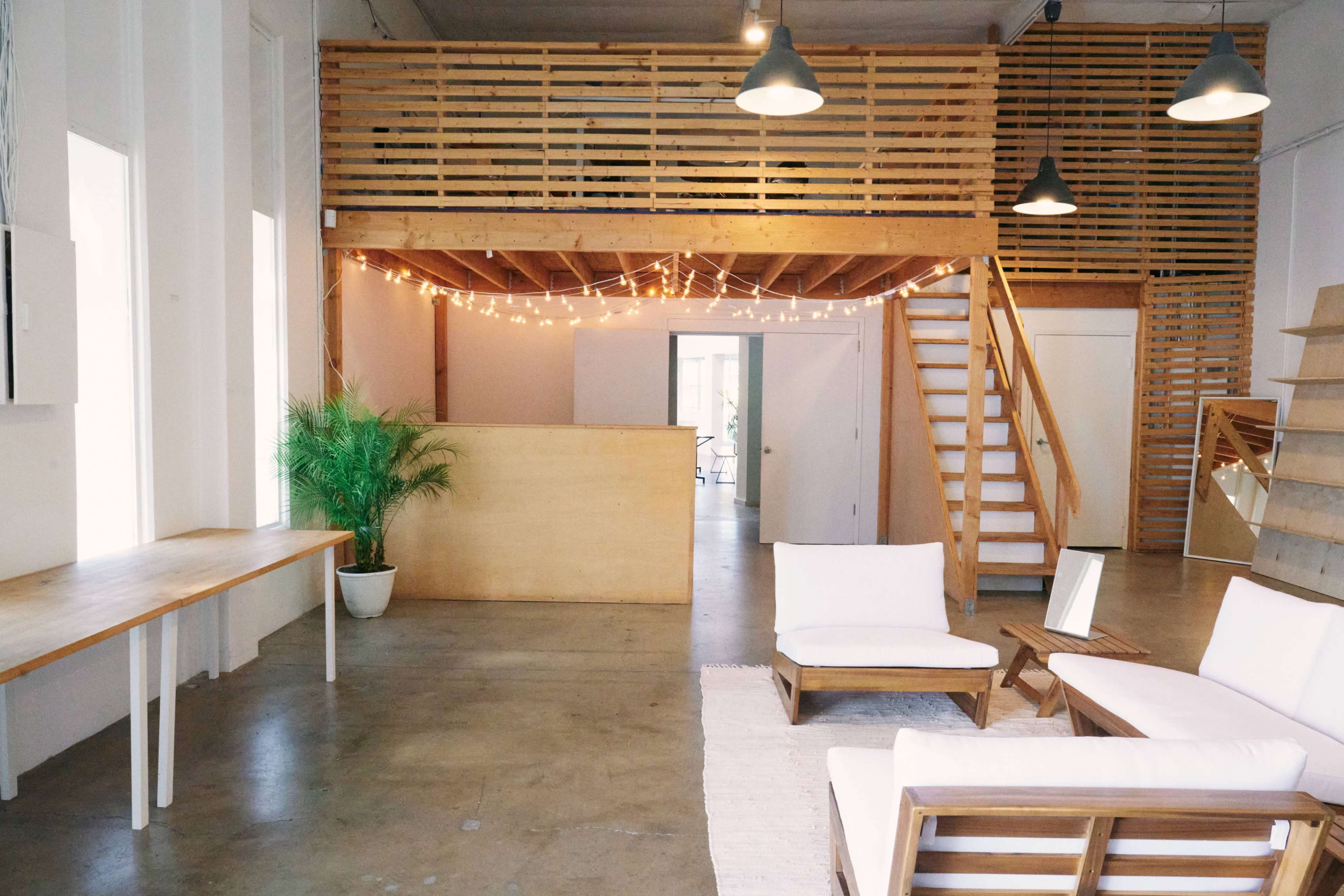 A spacious interior with a wooden loft, a reception area, and seating arrangements that include white couches and a small table.
