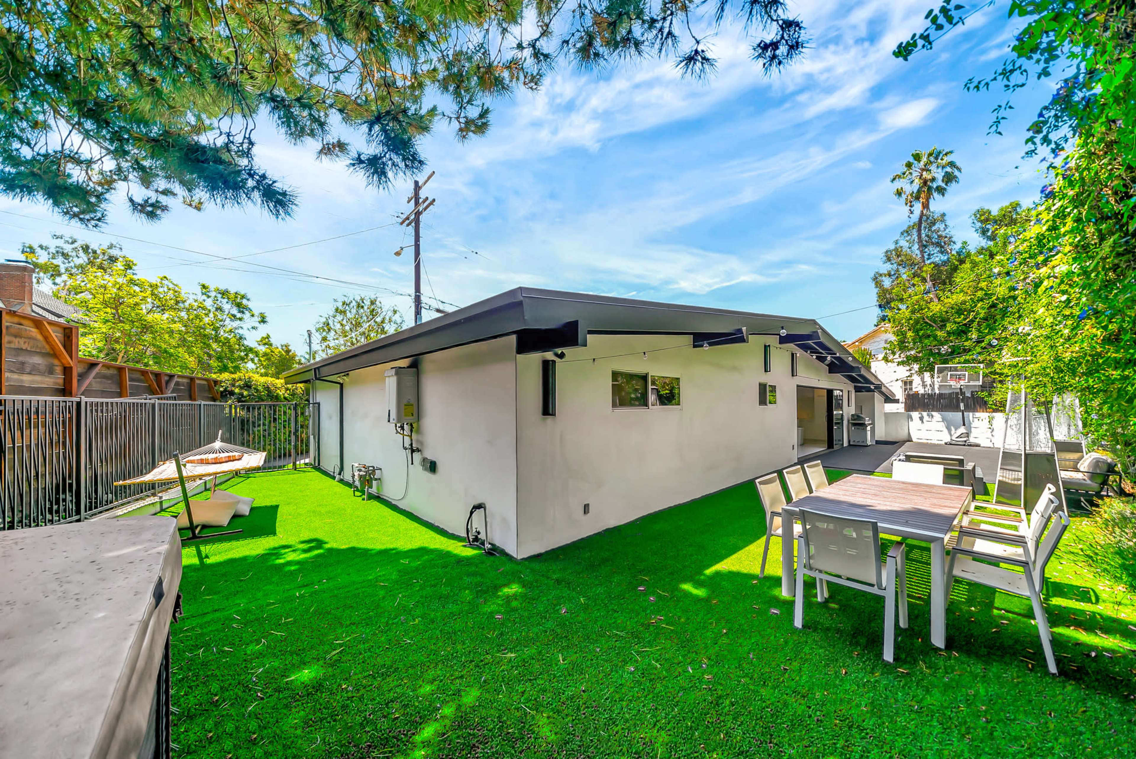 A modern house with a flat roof is surrounded by green artificial grass and features a dining set and basketball court in the backyard.