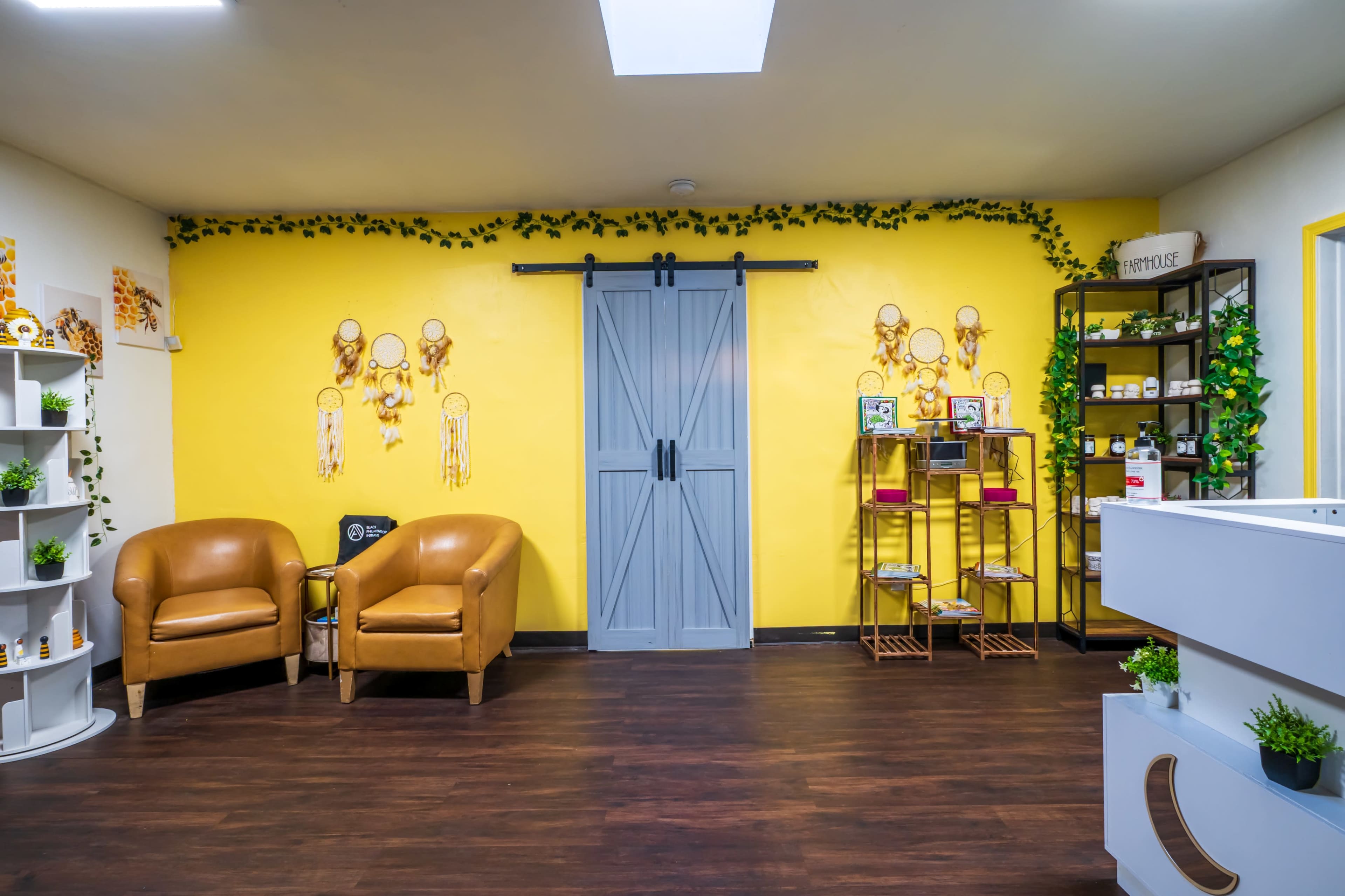 The image shows a cozy wellness room with yellow walls, two brown armchairs, a sliding gray door, and shelves displaying various items.