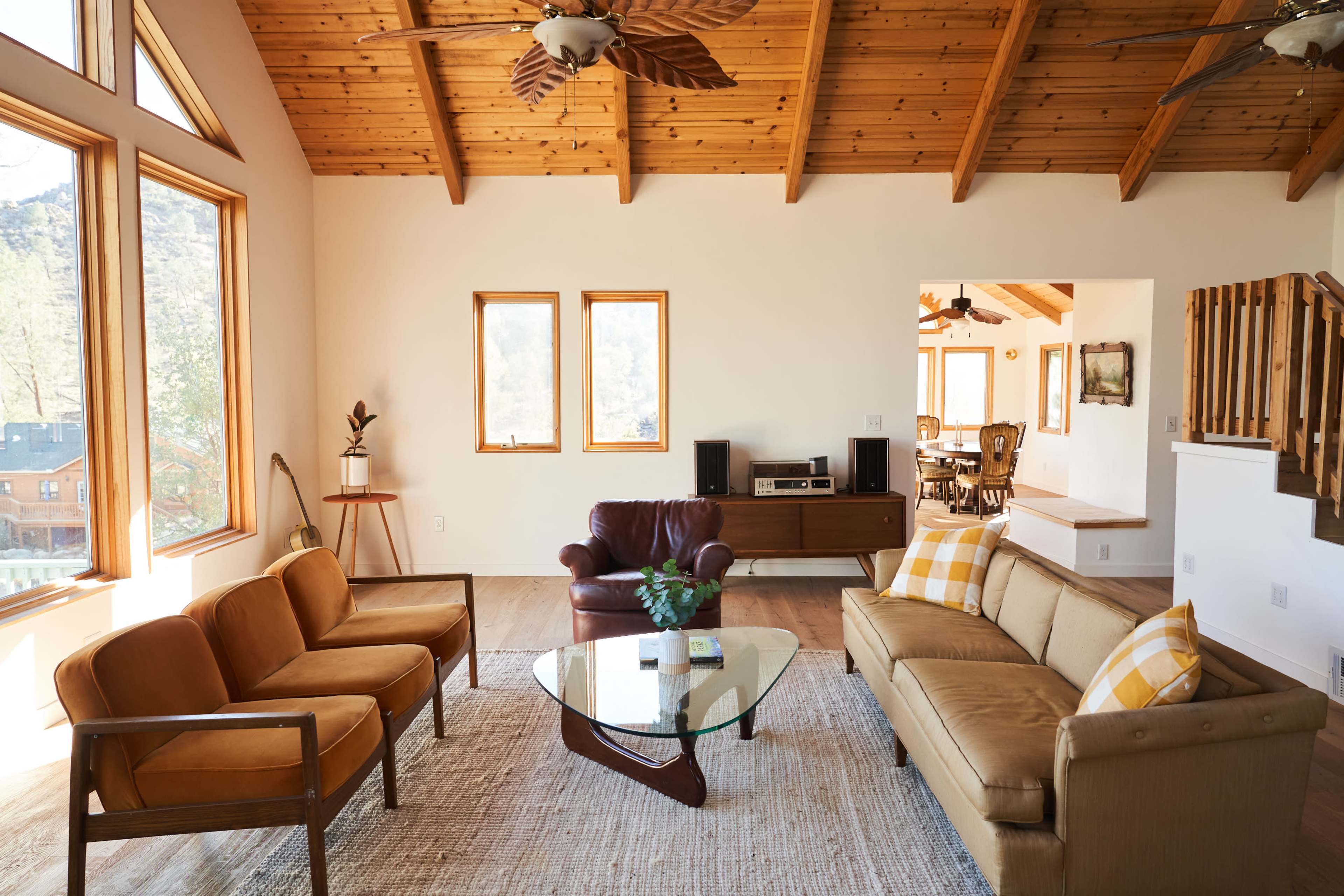 The living room features a combination of brown and beige furniture arranged around a glass coffee table under a wooden ceiling with exposed beams.