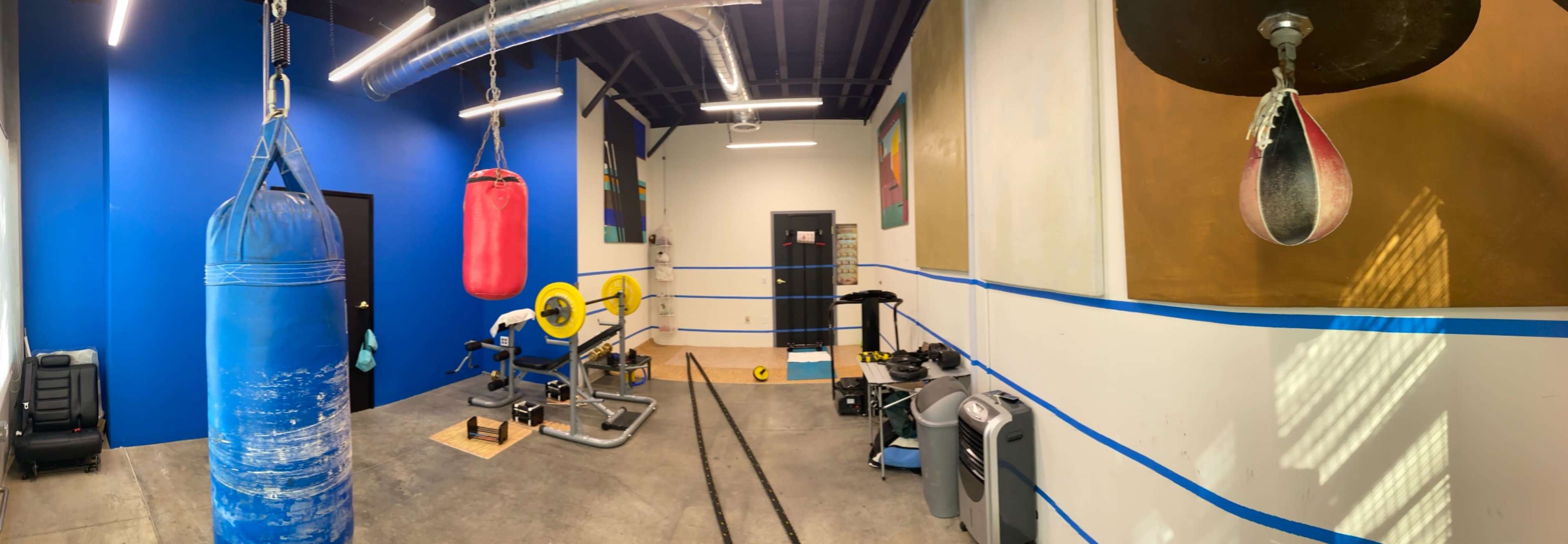 A fitness room equipped with a heavy bag, a speed bag, exercise equipment, and ropes along blue and white walls.